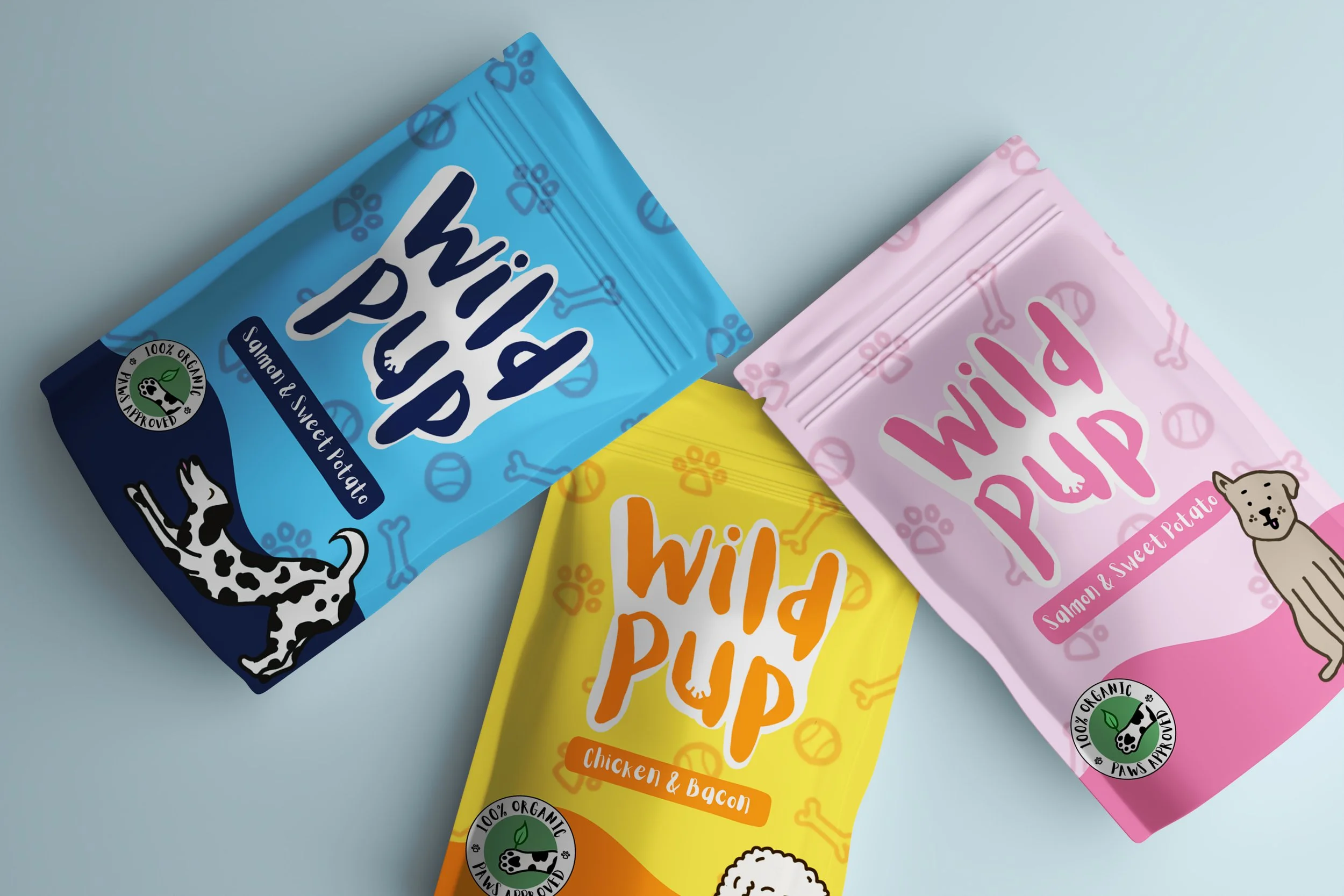 Three colorful packages of Wild Pup dog treats in blue, pink, and yellow, with dog illustrations and paw print patterns.