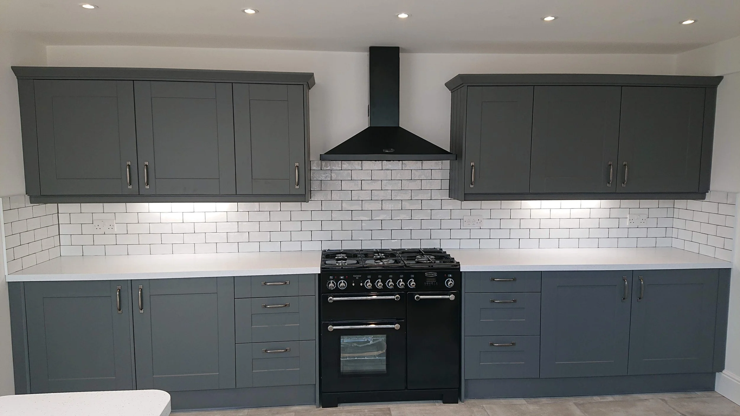 Kitchen with gray cabinets, white countertops, white subway tile backsplash, and a black stove with oven, including a black range hood above.