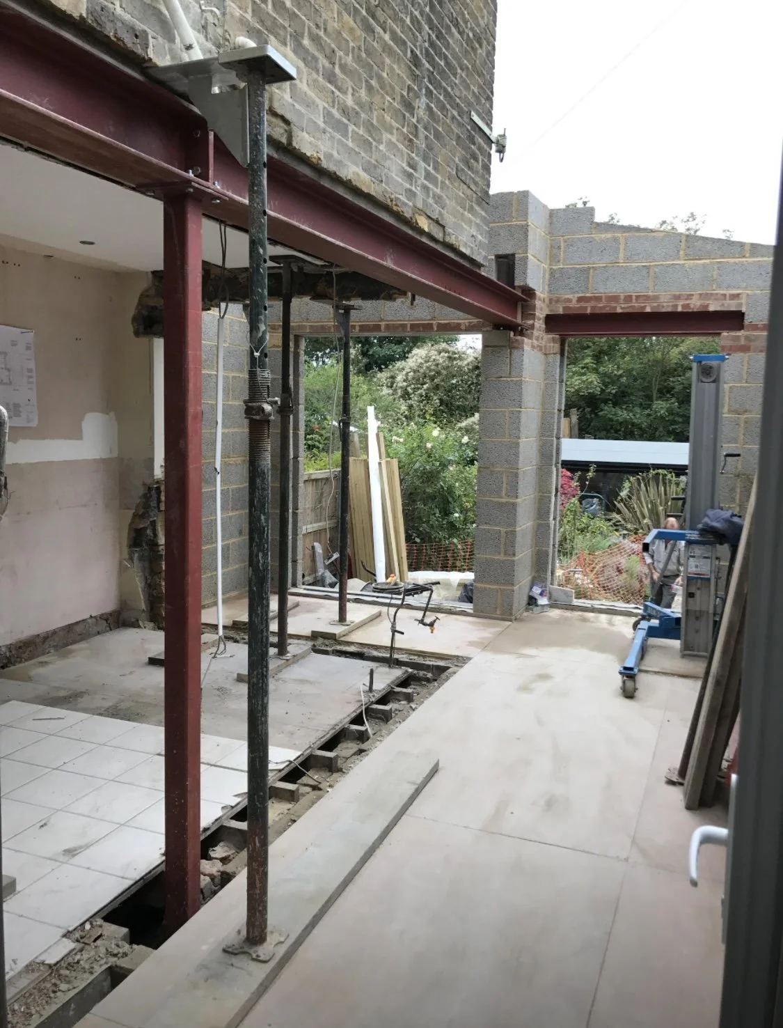 Construction site with scaffolding and brick walls in progress, partially tiled floor, construction tools, and materials in a backyard area.