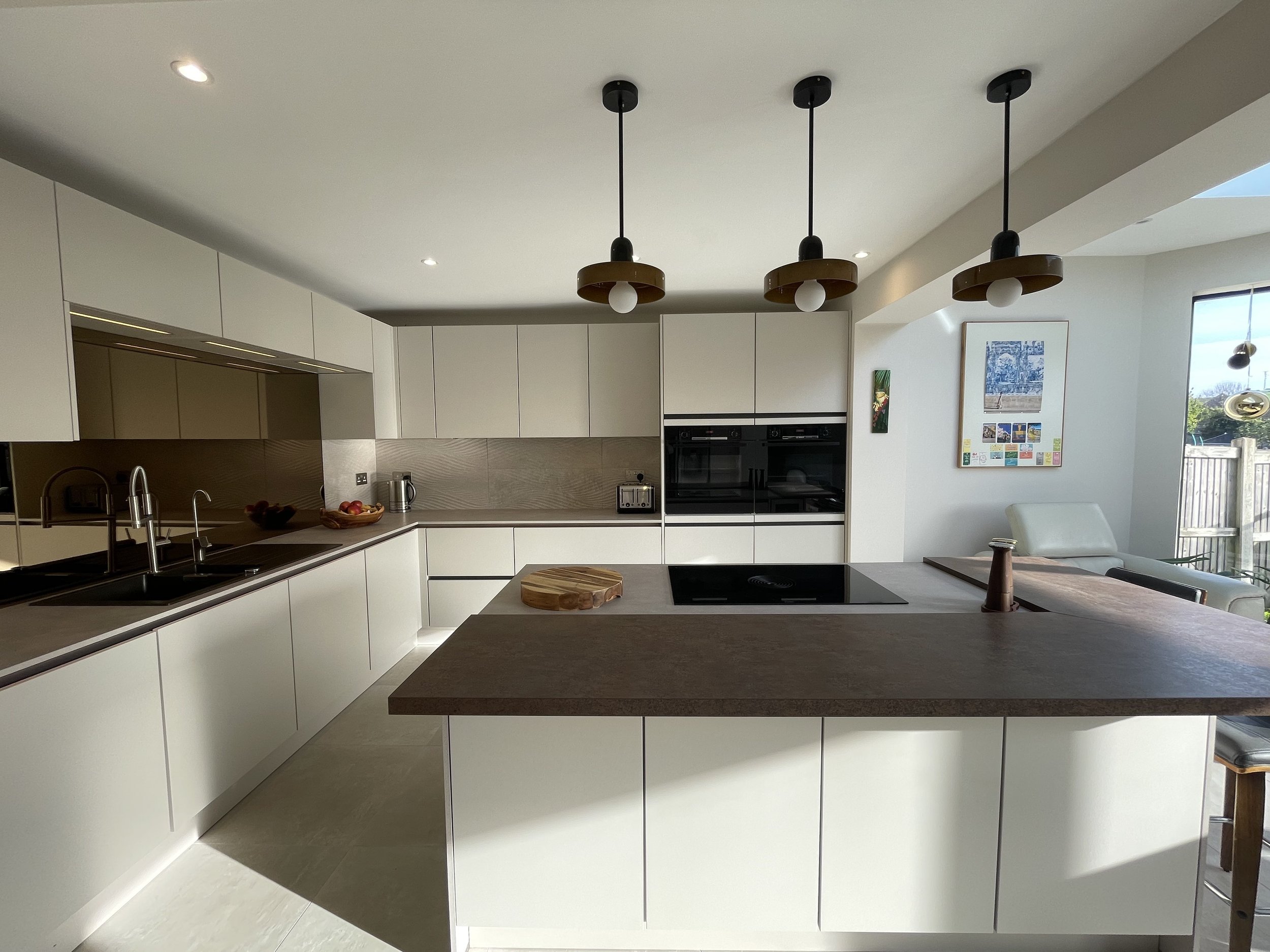 Modern kitchen with stone cabinets, black stovetop, wooden countertop island, and pendant lights, with a window overlooking a fenced backyard, Folkestone Kitchen renovation