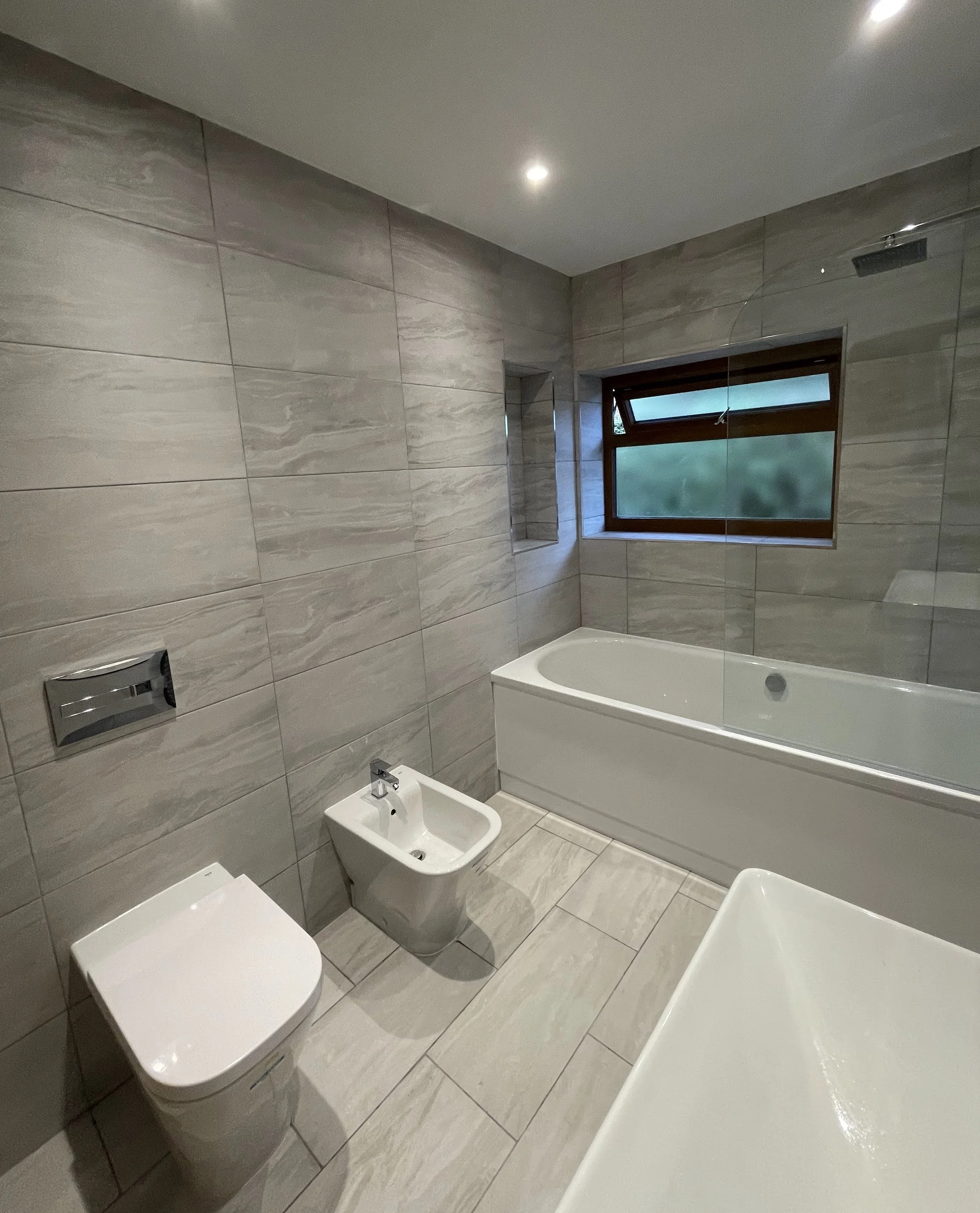Modern bathroom with beige tiled walls and floor, a bathtub, a window, and a bidet.