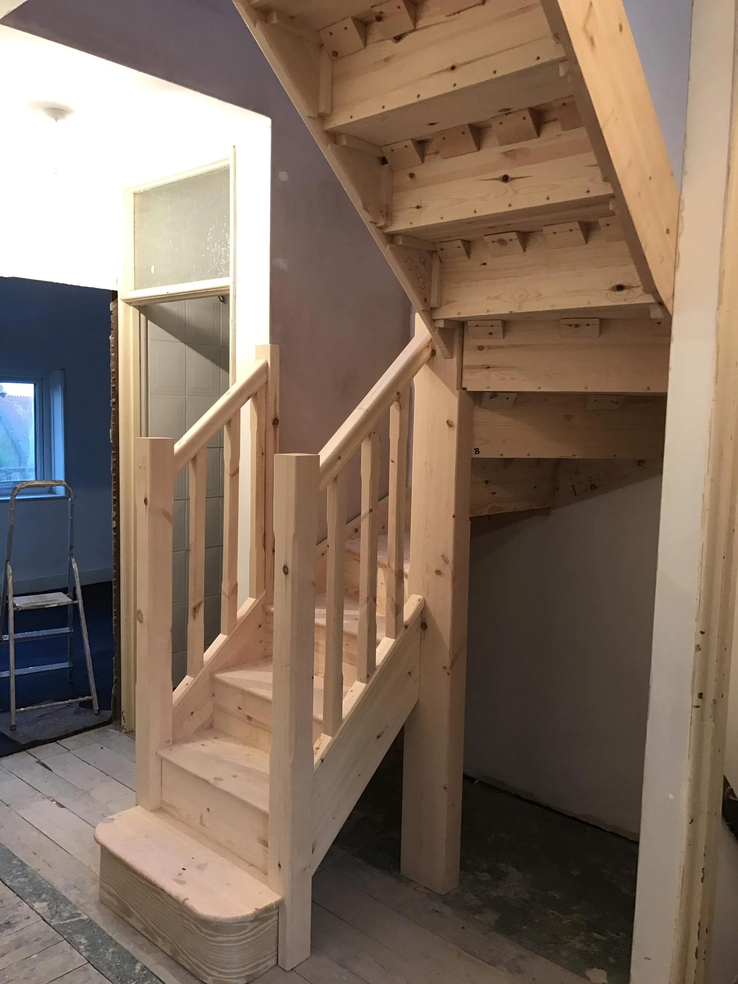 Wooden staircase under construction next to a wall, with unfinished steps and railing, in a home interior.