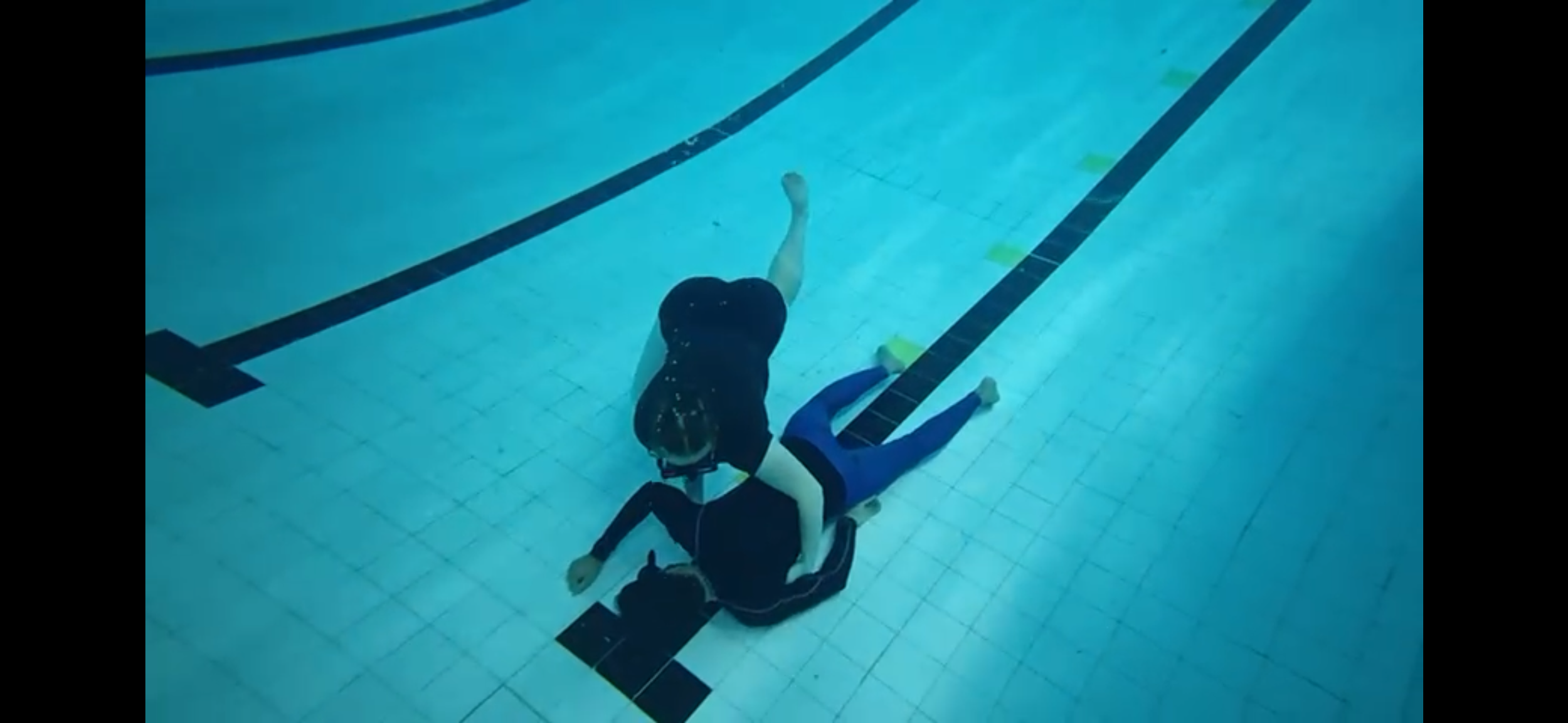 Child being rescued from the bottom of a swimming pool by an adult.