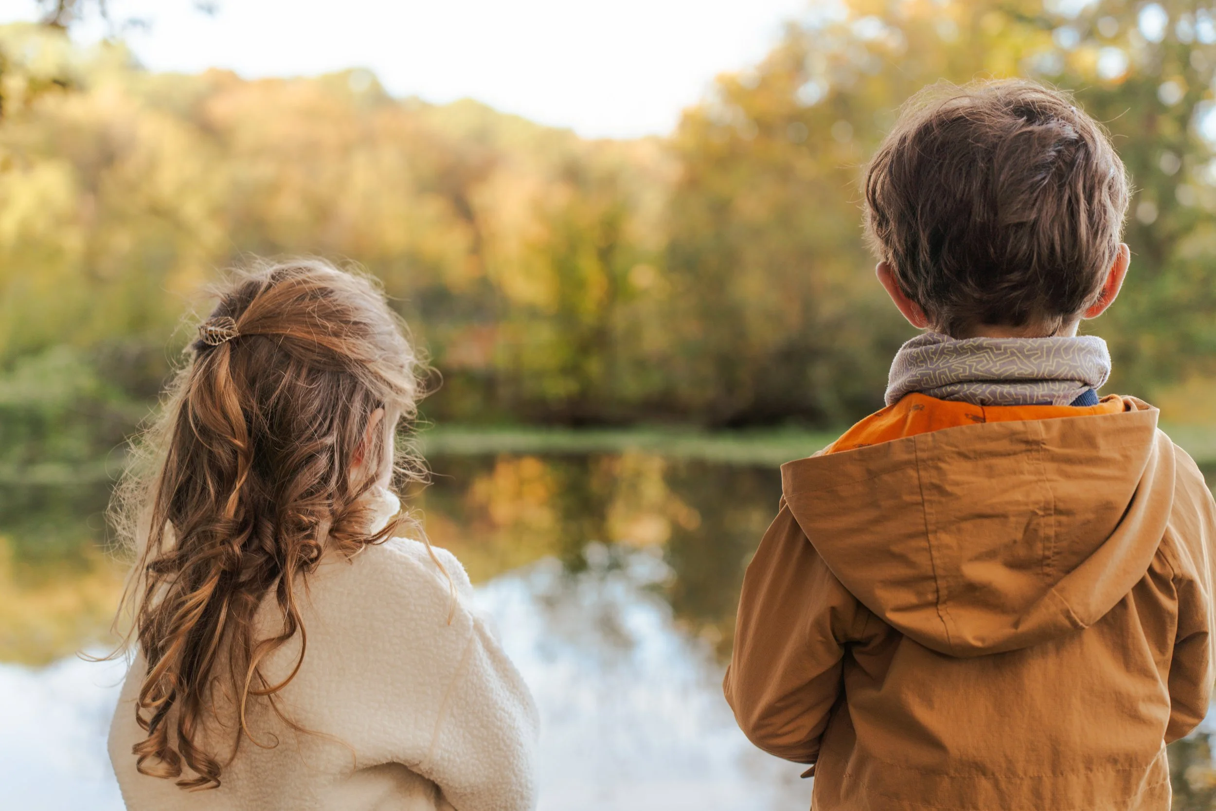 Deux enfants regardant un lac ou une rivière avec un arbre aux couleurs d'automne en arrière-plan.