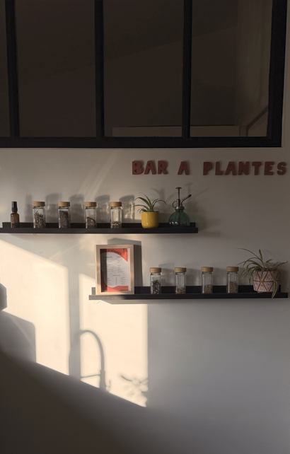 Deux étagères noires avec des pots de plantes et d'épices, une plaque signalétique "Bar à Plantes" en rouge