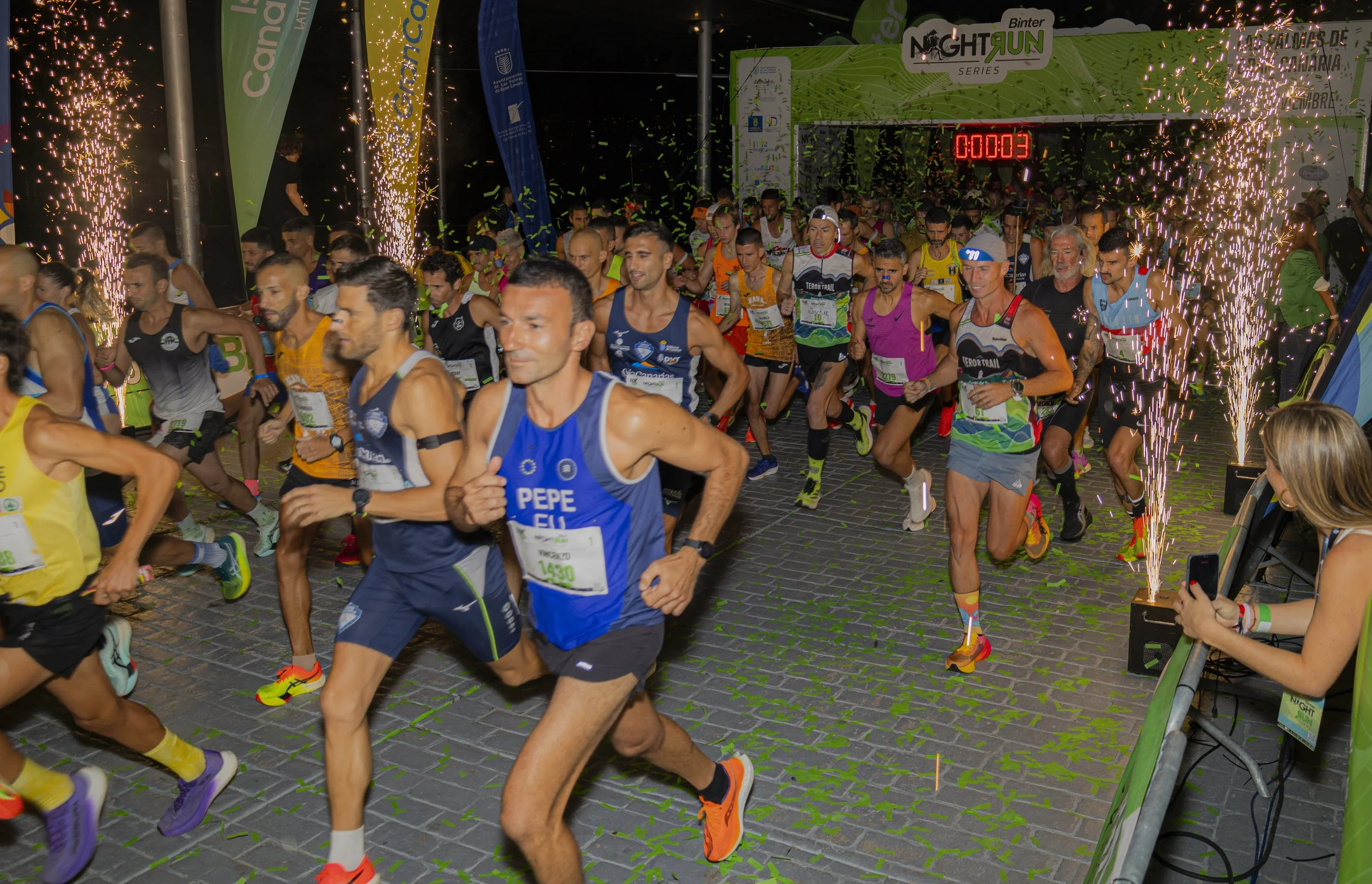 Corredores en la línea de salida en una carrera nocturna con fuegos artificiales y confeti.