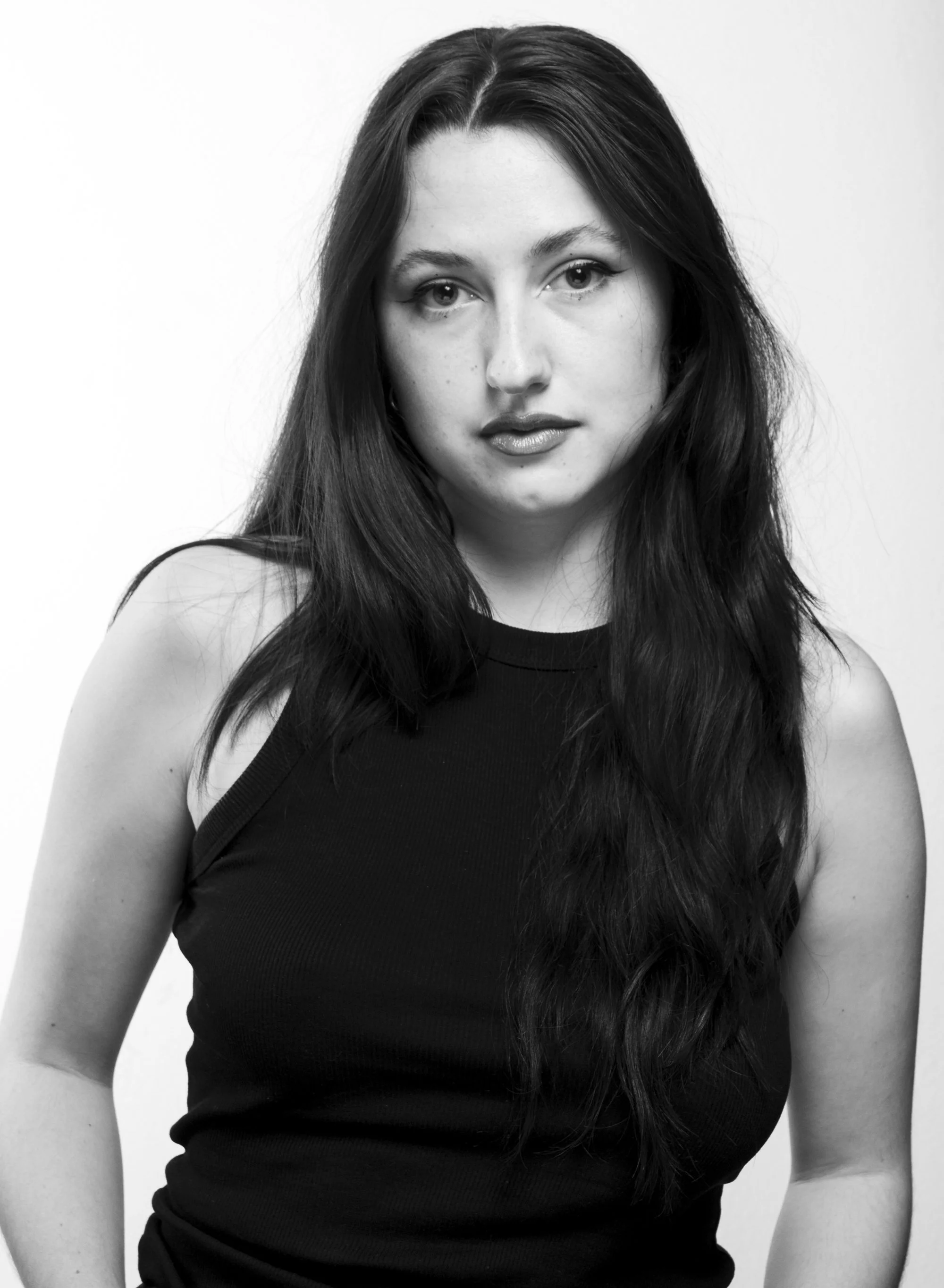 Retrato en blanco y negro de una mujer joven con cabello largo y oscuro, usando una camiseta sin mangas, mirando hacia la cámara.