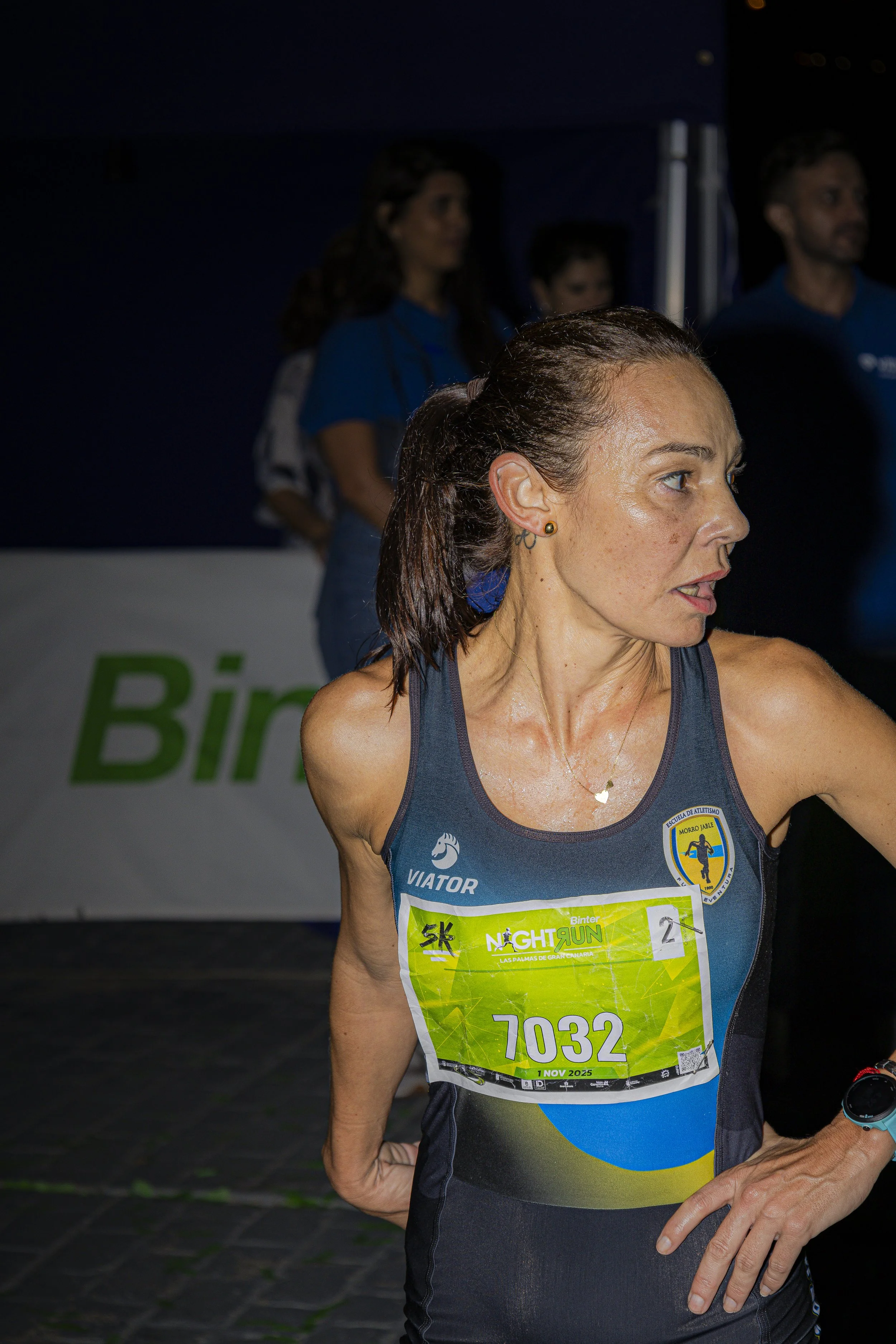 Mujer en una competición de running, con camiseta sin mangas y número de corredor 7032, en una carrera nocturna.