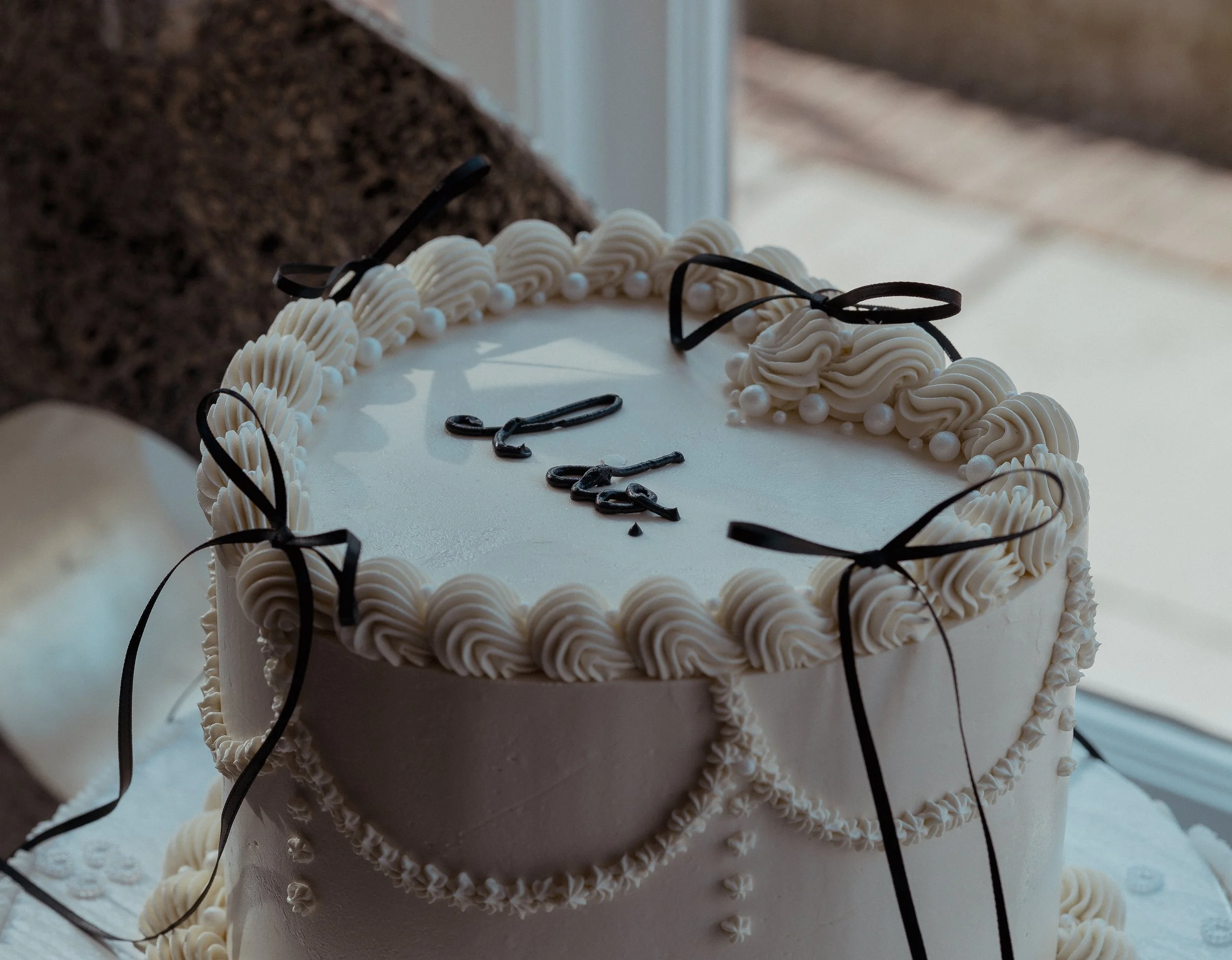 A white wedding cake decorated with piped icing, black ribbons, and the words 'I do' written on top.