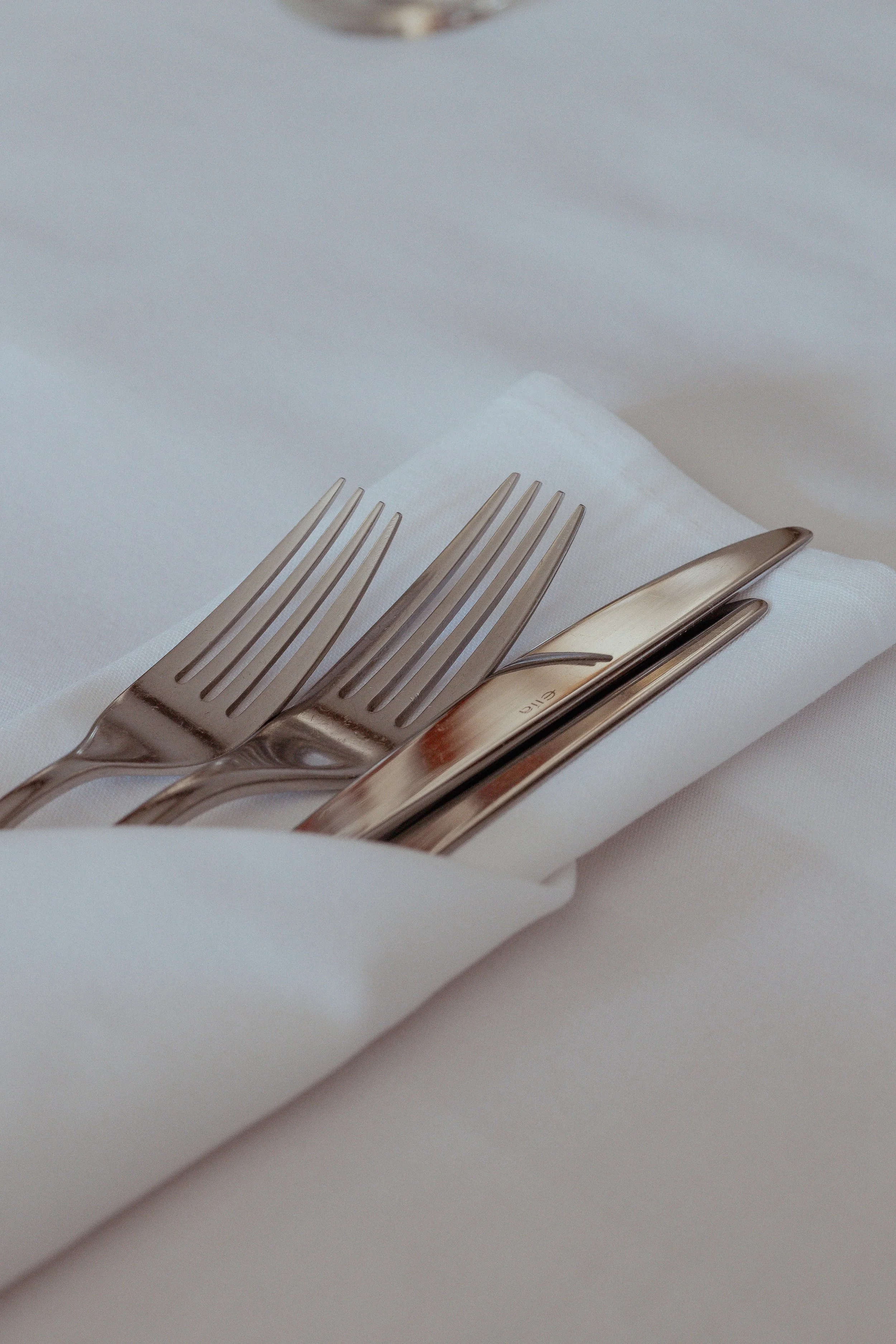 Two stainless steel forks and a butter knife resting on a white cloth napkin.