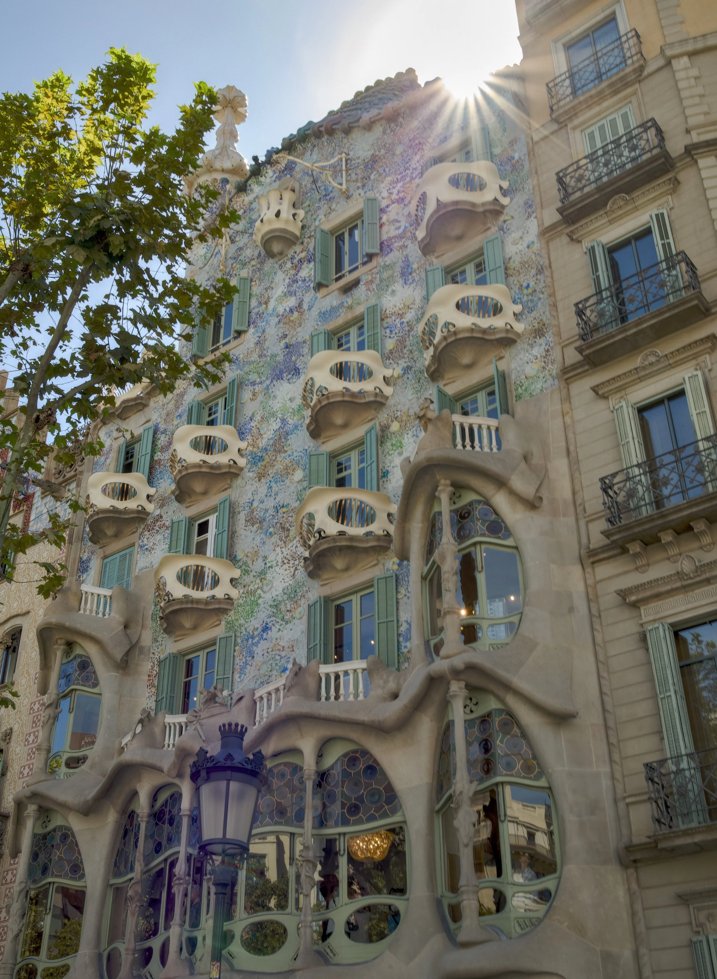 The exterior of Casa Batlló, a famous building designed by Antoni Gaudí in Barcelona, featuring organic shapes, colorful mosaics, and decorative balconies resembling skeletal structures.