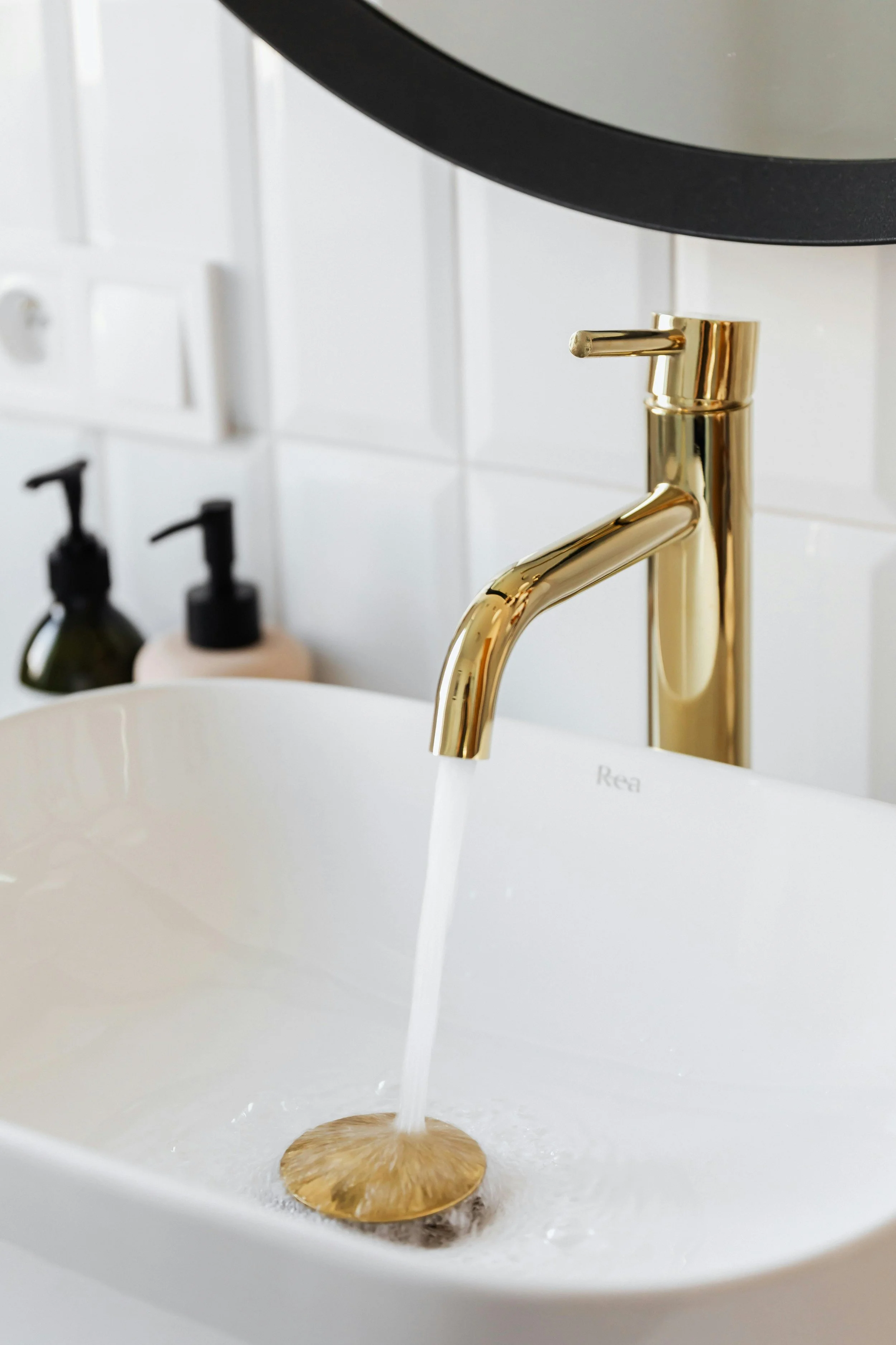 A white bathroom sink with a gold faucet, water flowing into the drain.