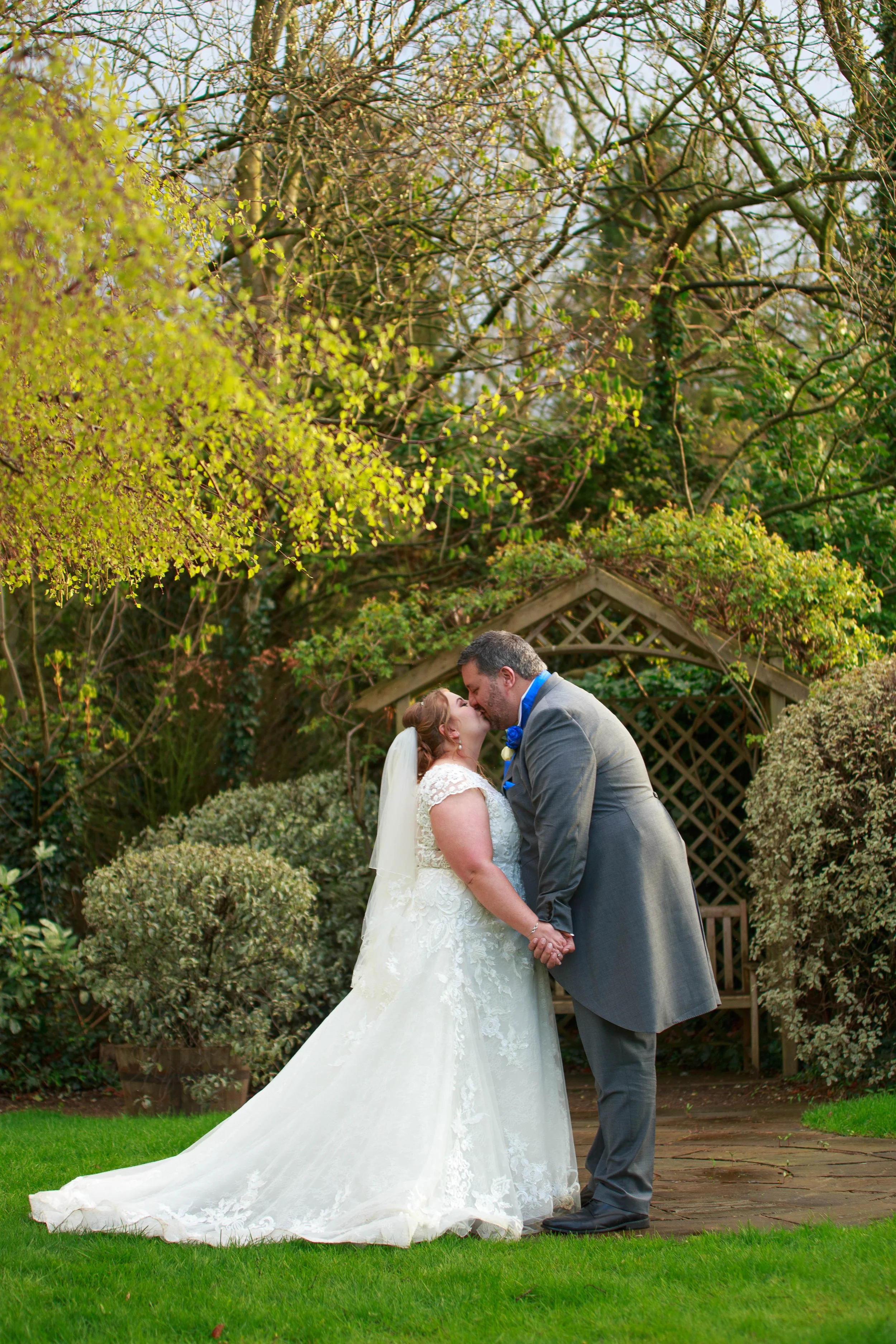 A bride and groom sharing a kiss and holding hands in a garden.
