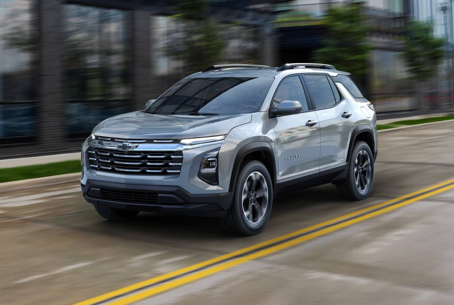 A silver Chevrolet SUV driving on a city street with a glass building in the background.