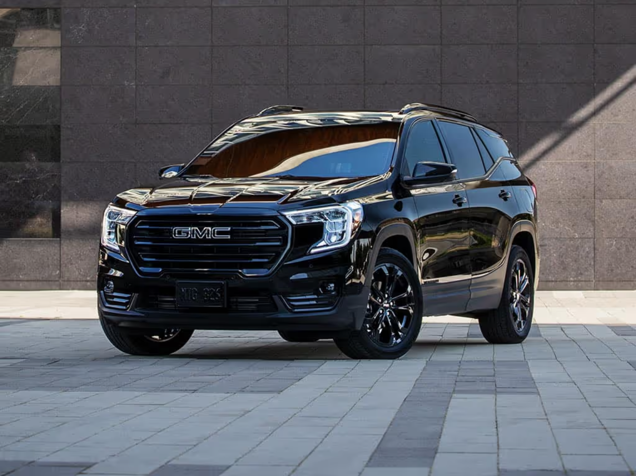 Black GMC SUV parked on a paved surface in front of a stone wall.