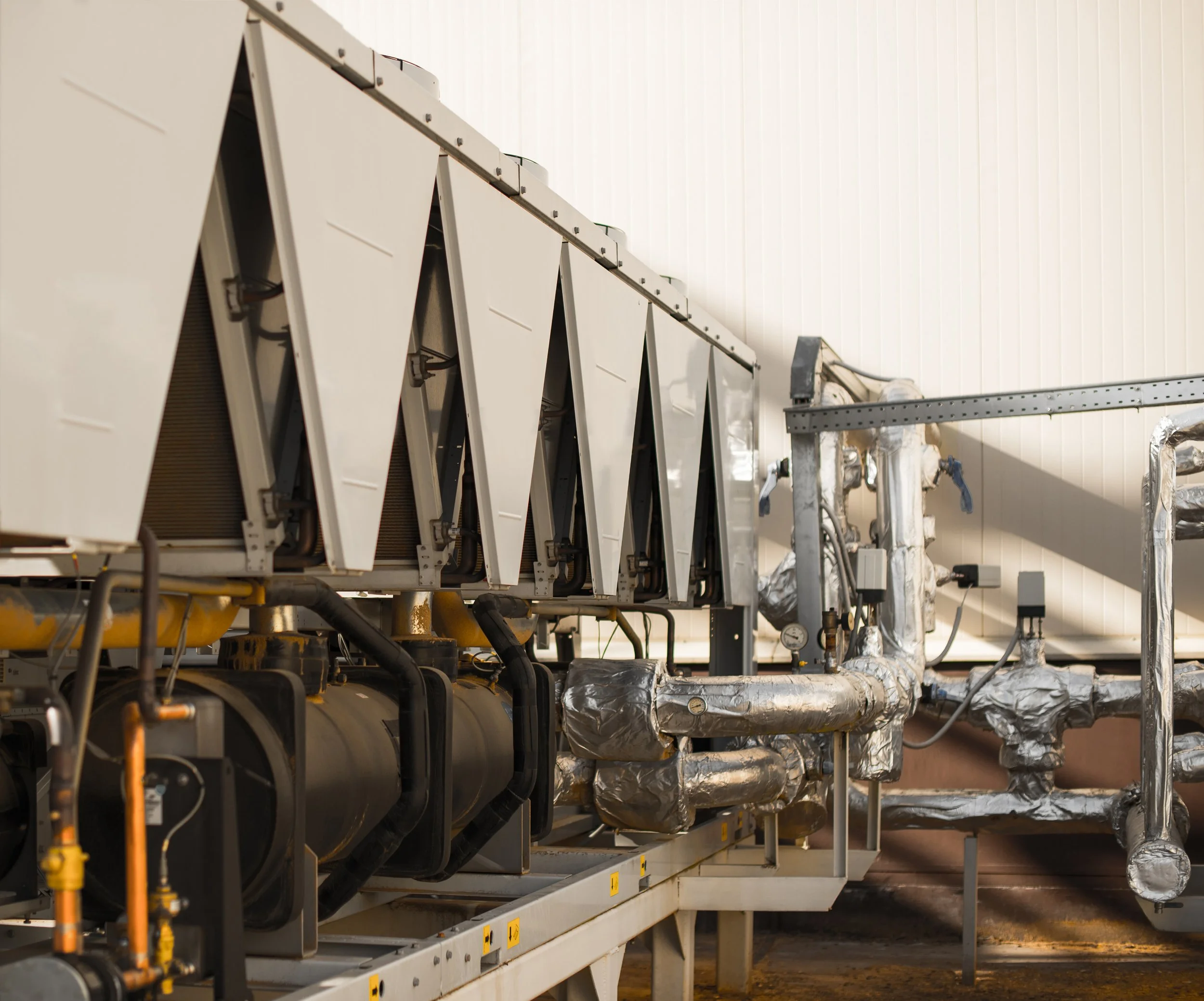 Industrial HVAC equipment with large white units, black pipes, and silver insulated ductwork in a factory setting.