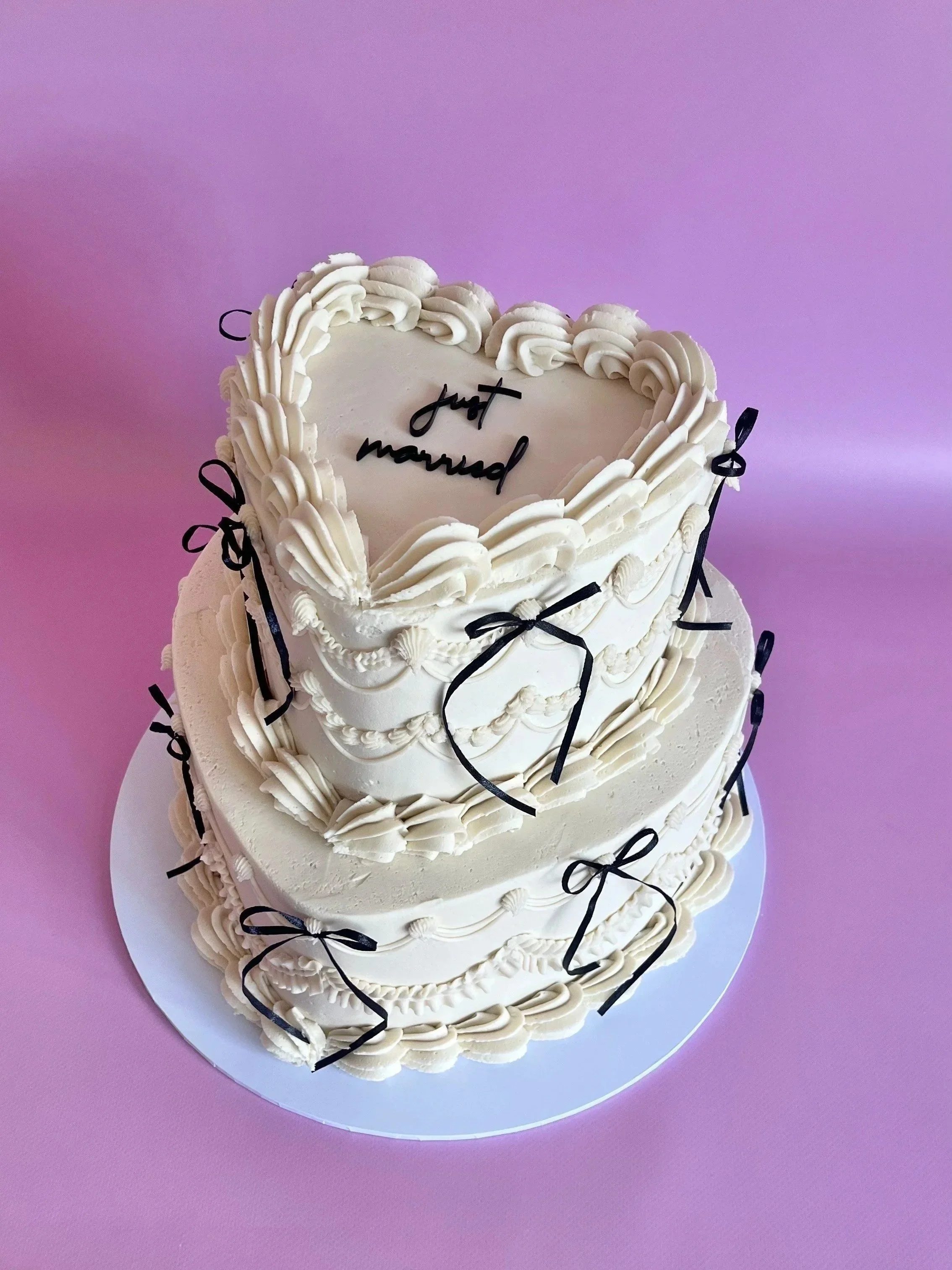 A two-tiered white wedding cake decorated with black ribbon bows