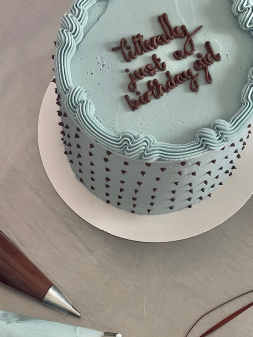 A round birthday cake with light blue buttercream, decorated with brown buttercream.