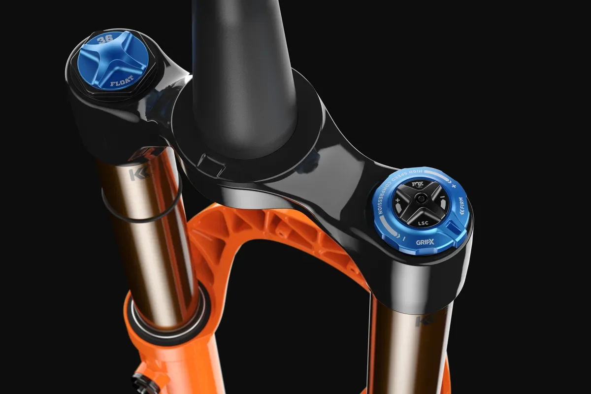 Close-up van een mountainbike voorkopvork met blauwe en oranje onderdelen tegen een zwarte achtergrond.