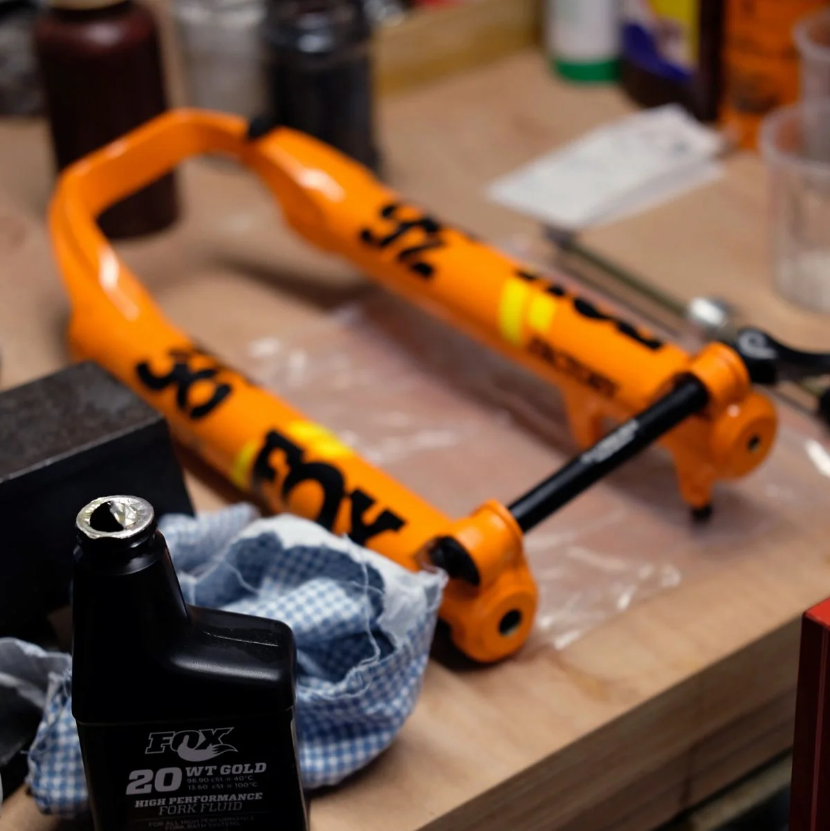 Een oranje fietsvoorvork met zwarte en gele markeringen ligt op een werkbank, omringd door gereedschap en smeermiddelen.
