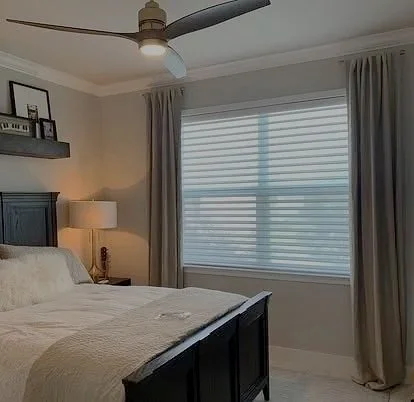 A bedroom with a bed, nightstand, reading lamp, curtains, and a window with blinds and drapes.
