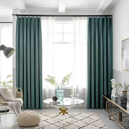 Living room with teal drapes, a round white table, a beige pouf, a black side table, and decorative plants.