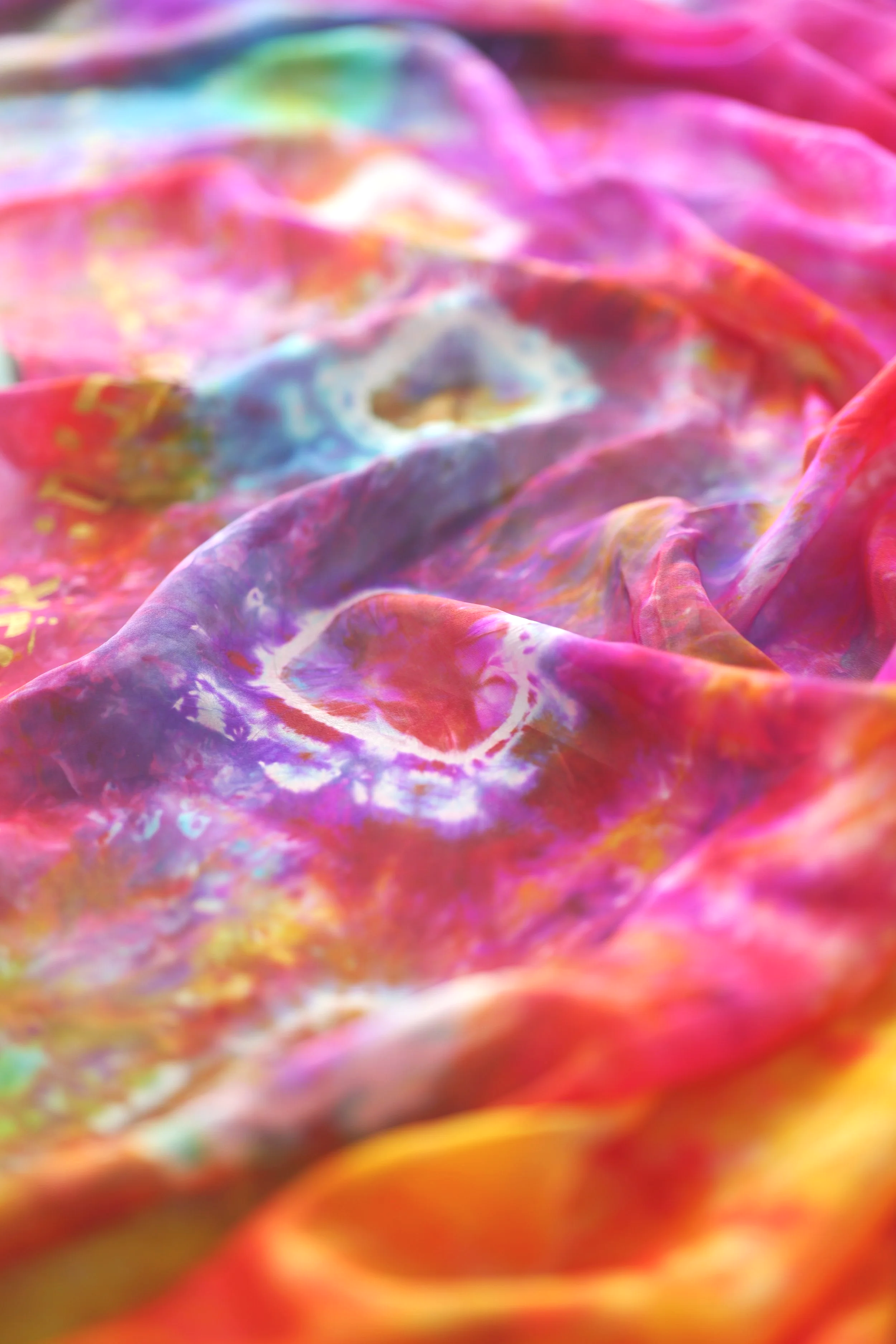 Close-up of a colorful, tie-dye cloth with bright pink, purple, yellow, and blue hues and circular patterns.