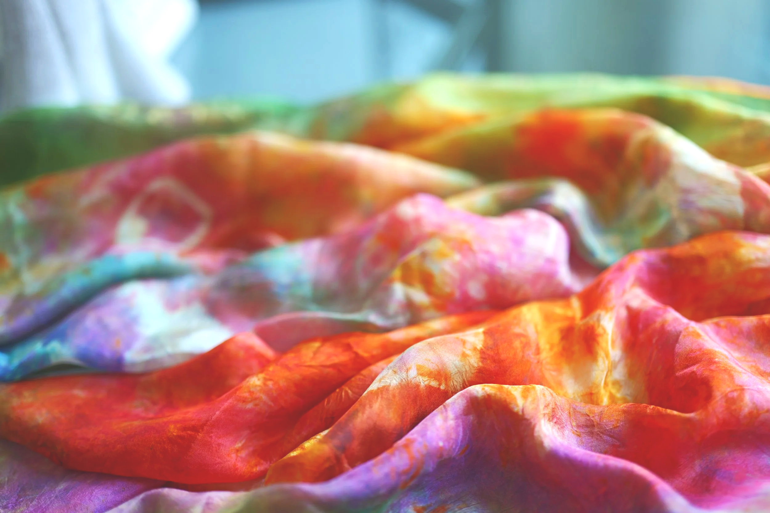 Close-up of a multicolored tie-dye fabric with vibrant pink, orange, purple, and green hues, draped and wrinkled.