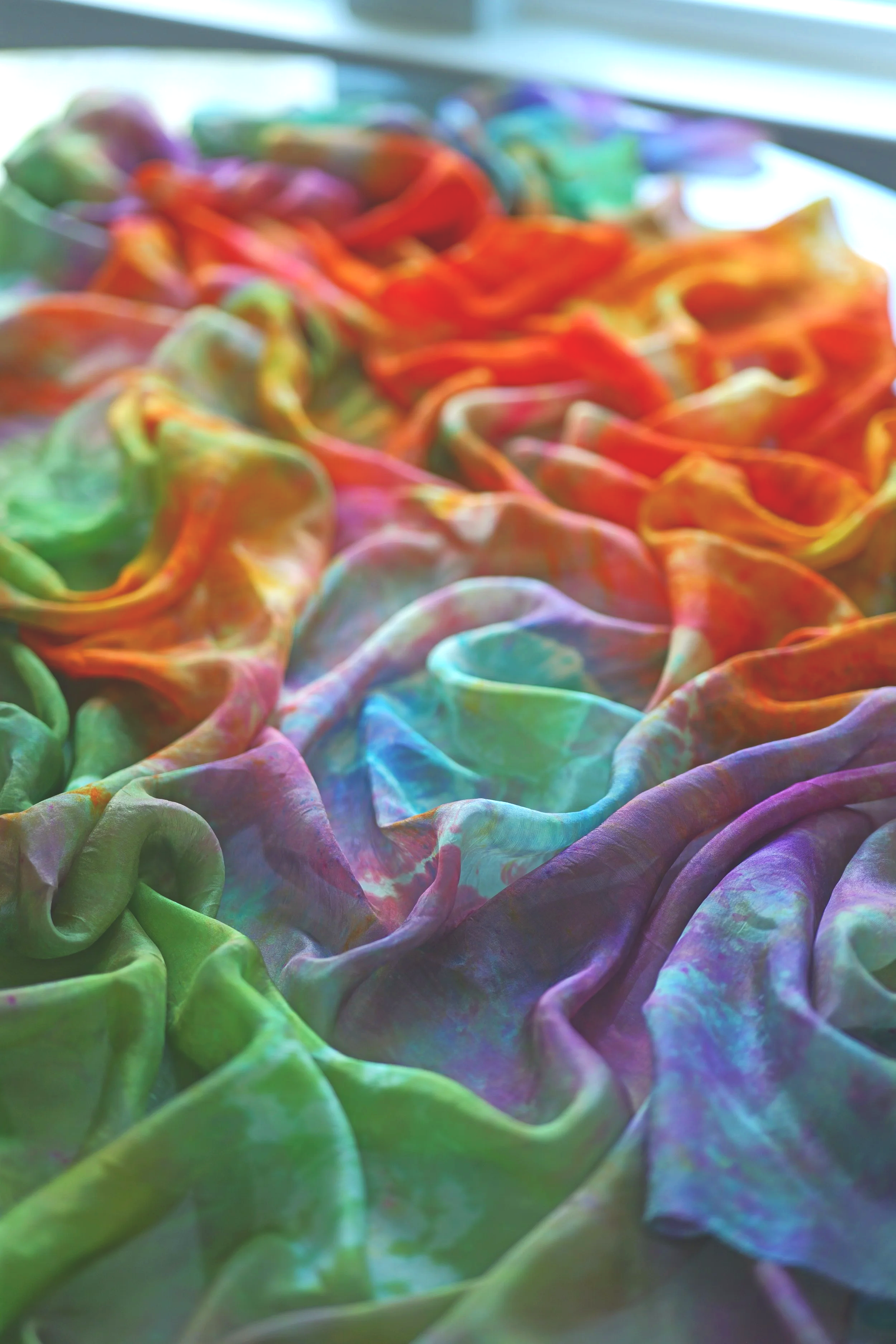 Close-up of colorful, tie-dye patterned fabric in shades of green, purple, pink, blue, and orange, arranged with soft folds.