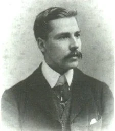 Black and white portrait of a man with a mustache, wearing a suit and tie.