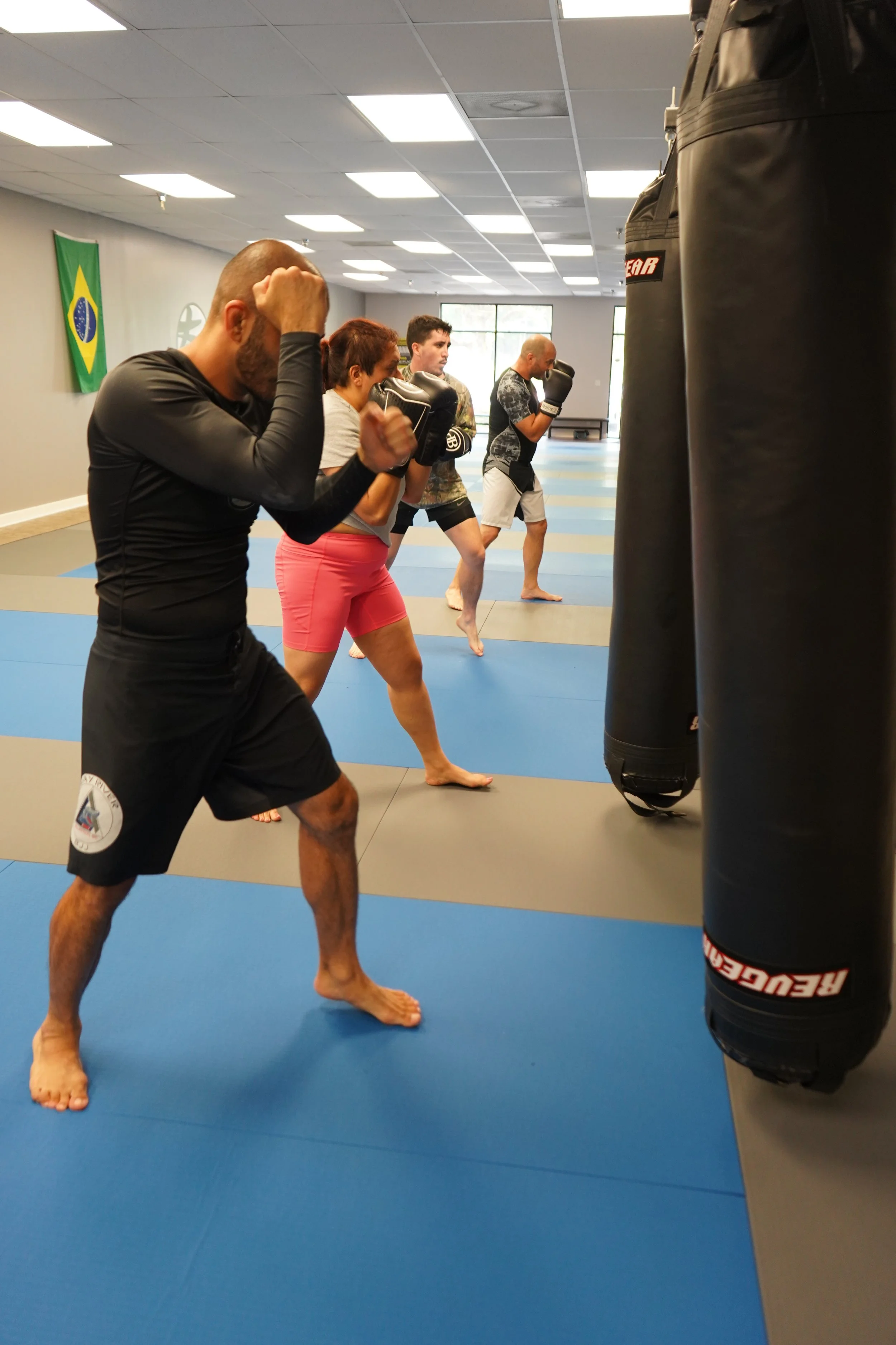 Group of four people practicing boxing on a gym floor with punching bags.