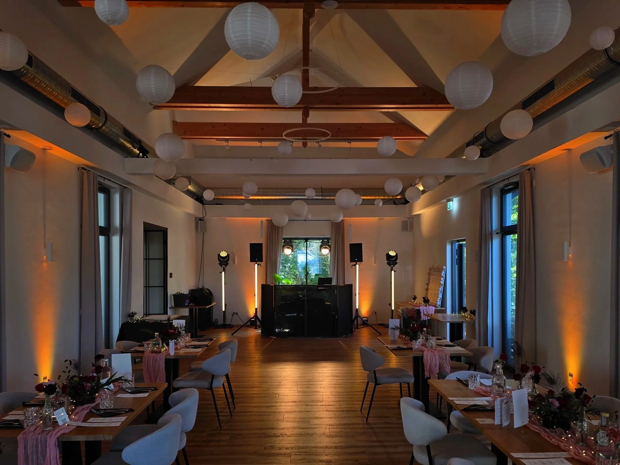Wedding reception area with DJ setup including speakers, DJ equipment on a black table, and seating with tables and white chairs.