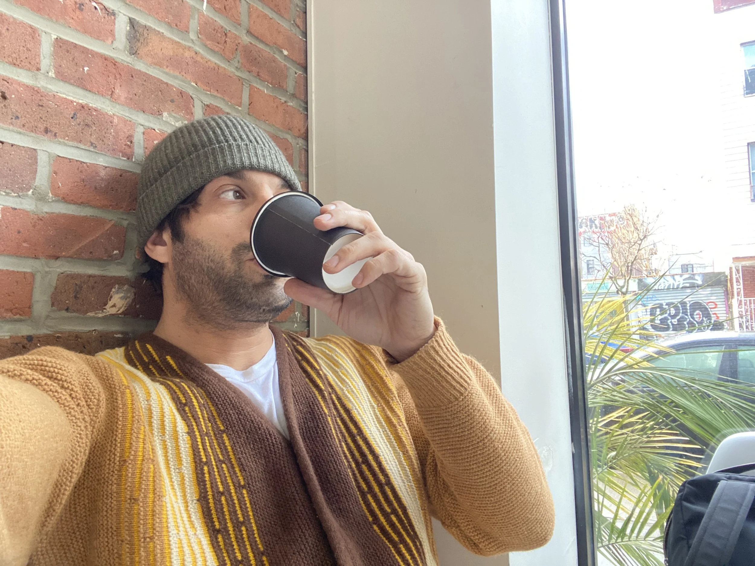 Alex Regen, creative entrepreneur and AI founder, enjoying coffee while working in a Brooklyn cafe