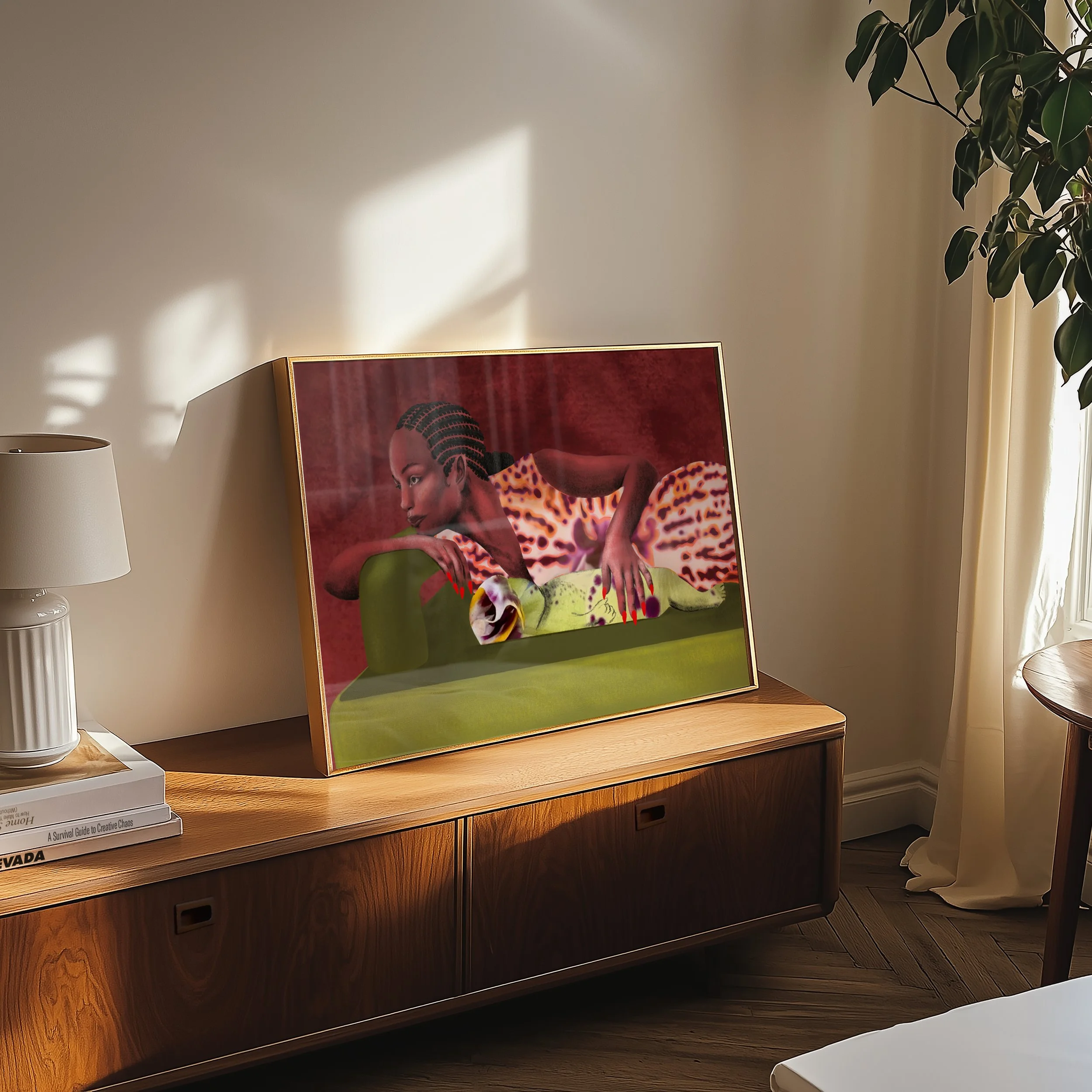 Interior of a room with a wooden sideboard, a framed colorful portrait of a woman with braided hair, a white table lamp, and a stack of books including one titled "A Survival Guide to Creative Chaos." A large green leafy plant is on the right side ne