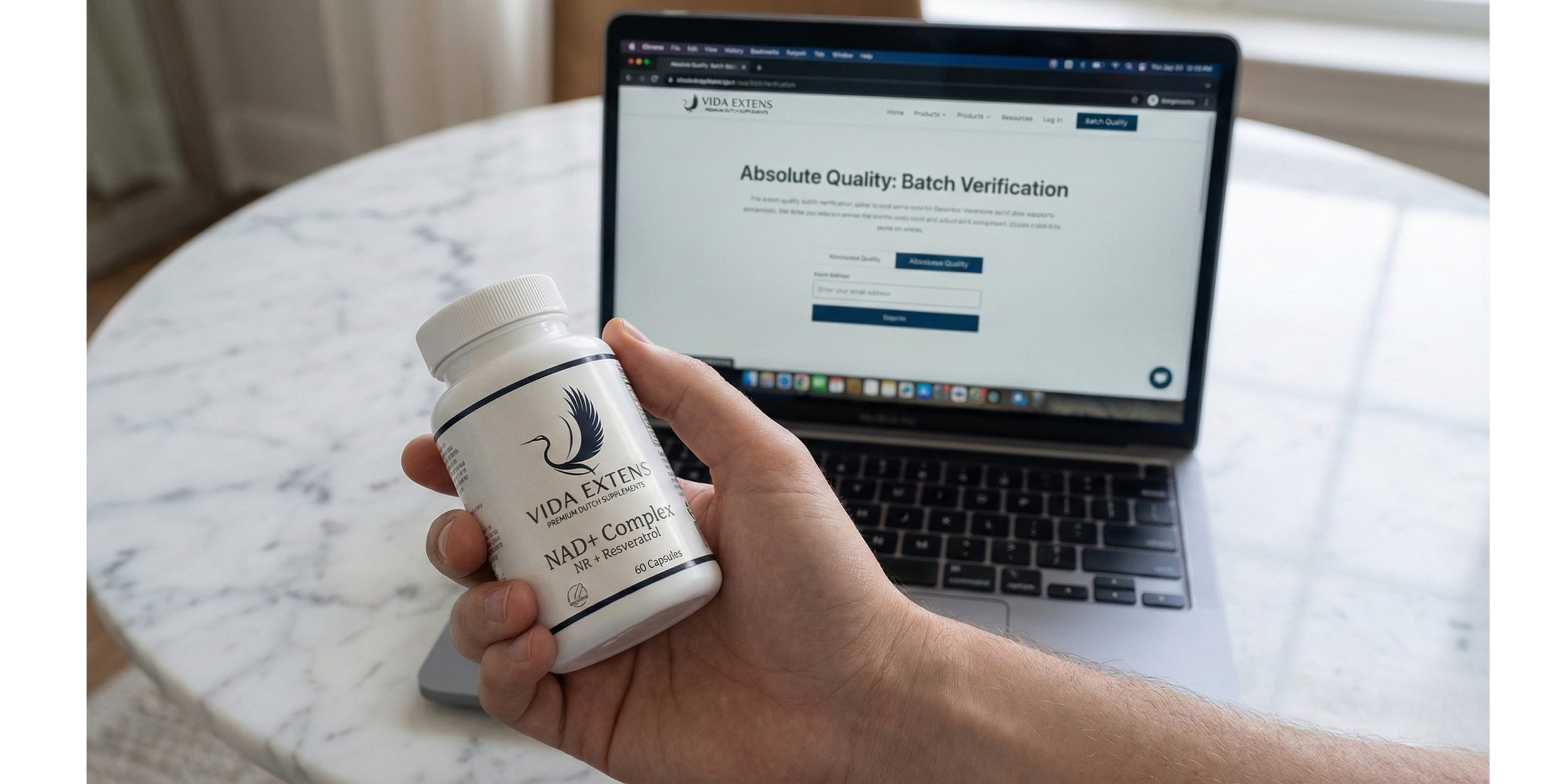 Persoon houdt een fles vitaminesupplementen vast terwijl op de achtergrond een open laptop staat op een marmeren tafel.