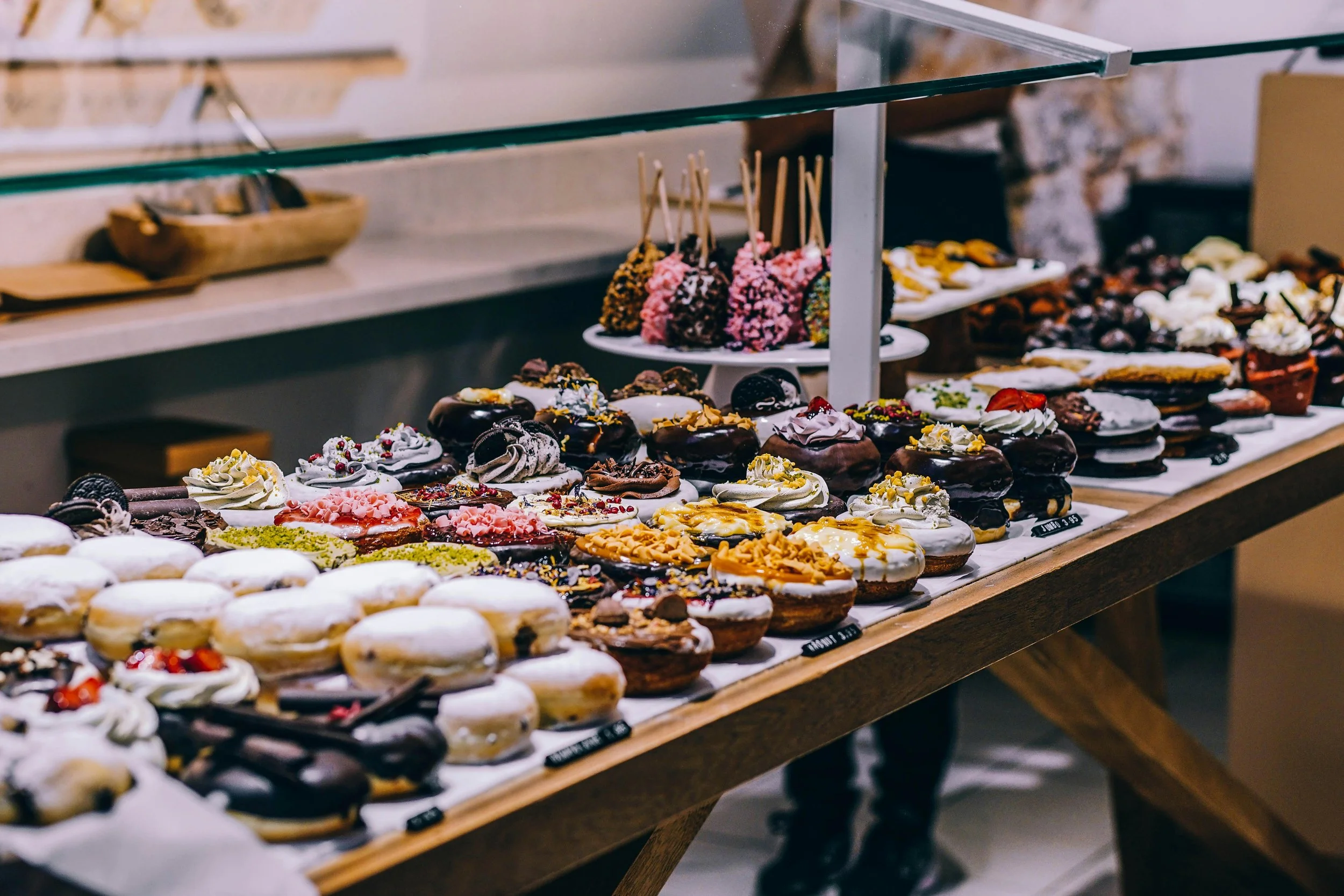 Variedad de donas decoradas con diferentes coberturas y glaseados, en una mesa de panadería.