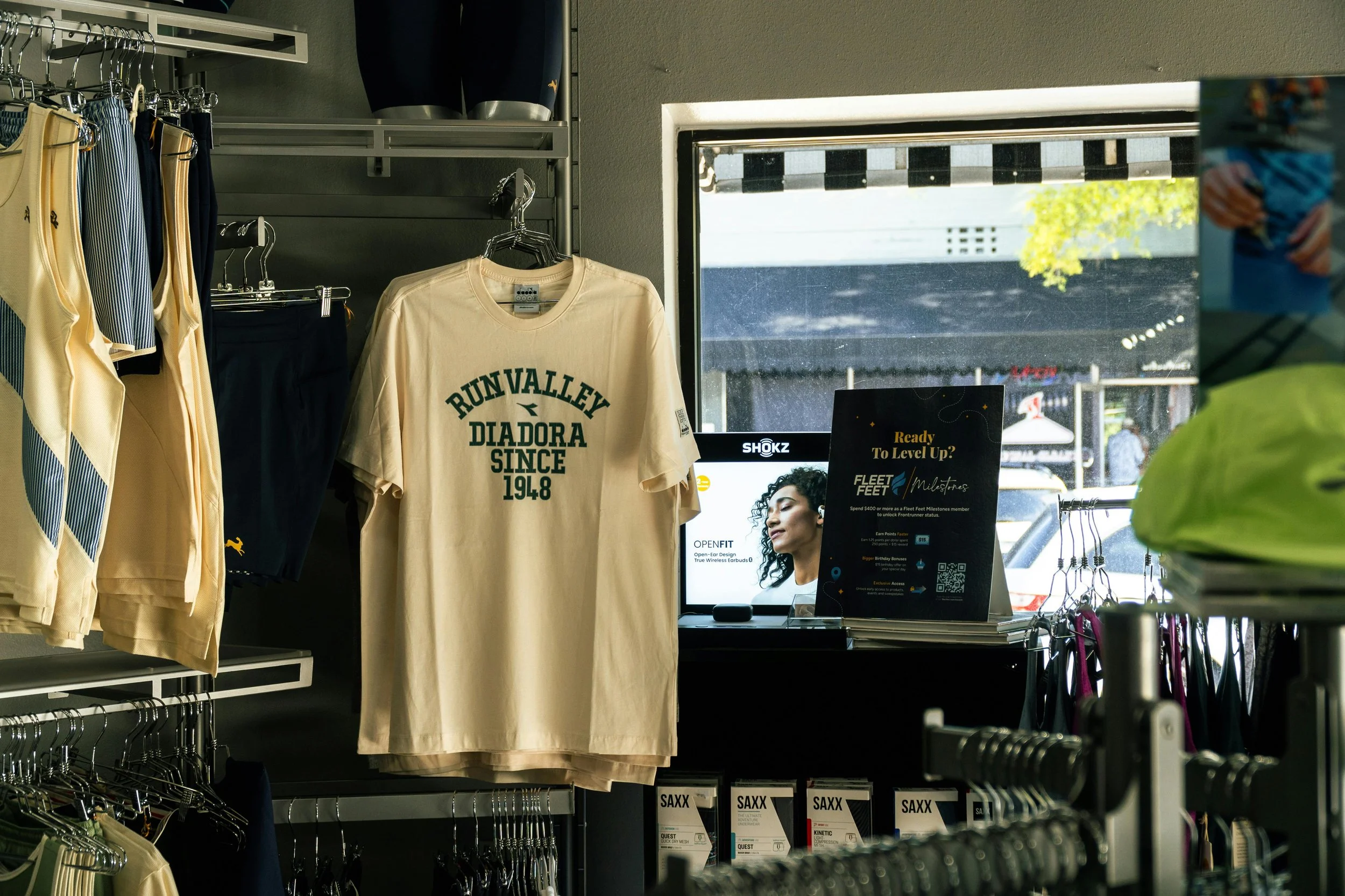 Vestido, camisetas y accesorios deportivos en una tienda con ventana al exterior y publicidad en exhibición.