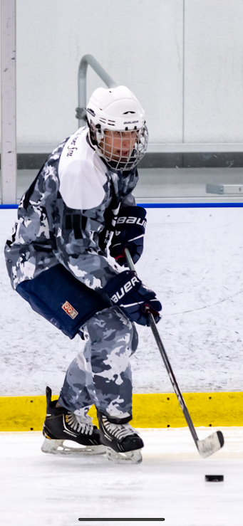 A young hockey player in camouflage jersey and shorts, wearing a white helmet, practicing ice hockey in an indoor rink in Lewis Center Ohio
