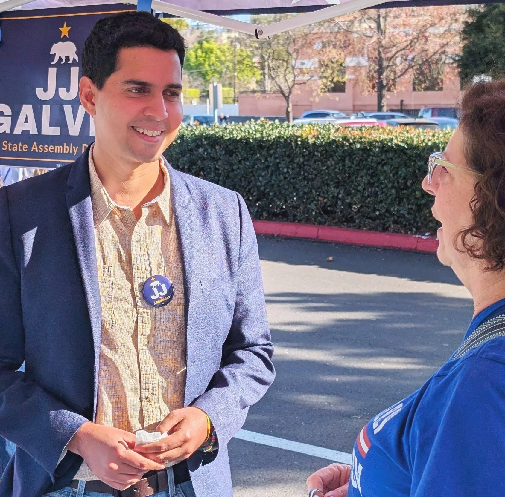 JJ Galves dressed in a yellow button down shirt and blue blazer talks with a woman at a campaign event for California State Assembly.