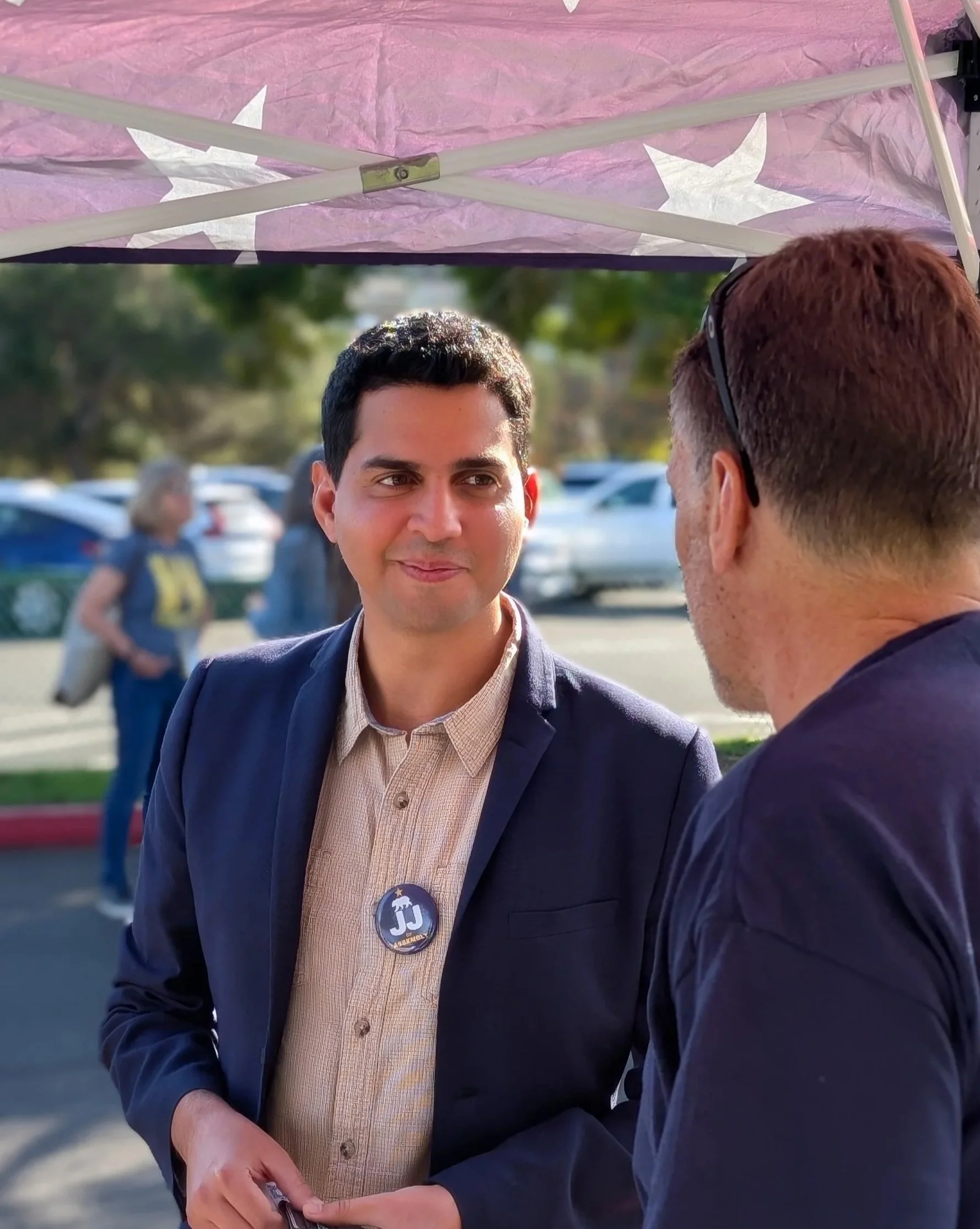An image of JJ Galvez, wearing a button down shirt and blue blazer, talking with a man at a campaign event for California State Assembly District 71.