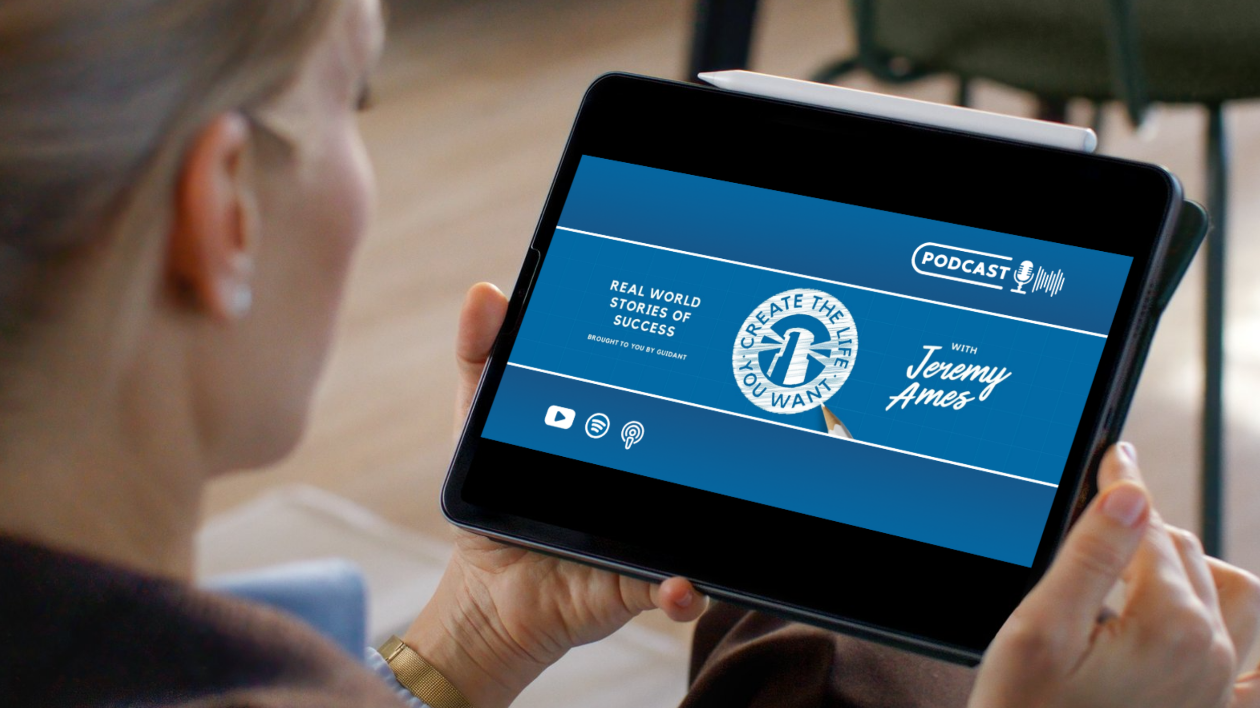 A person holding a tablet displaying a podcast cover with a blue background, a circular logo with a pencil, and text including "Create the Life You Want" and "Jeremy Ames".