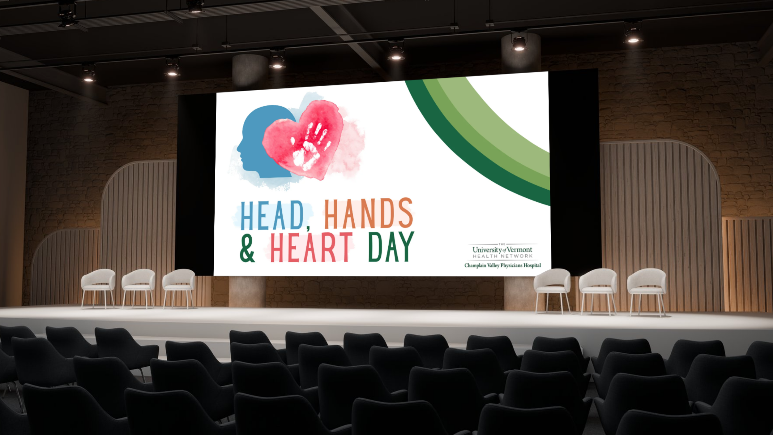 Large stage with a screen displaying a logo for 'Head, Hands & Heart Day,' featuring a blue human head outline with a pink heart-shaped handprint overlay, and text indicating it is organized by the University of Vermont Health Network and Champlain V