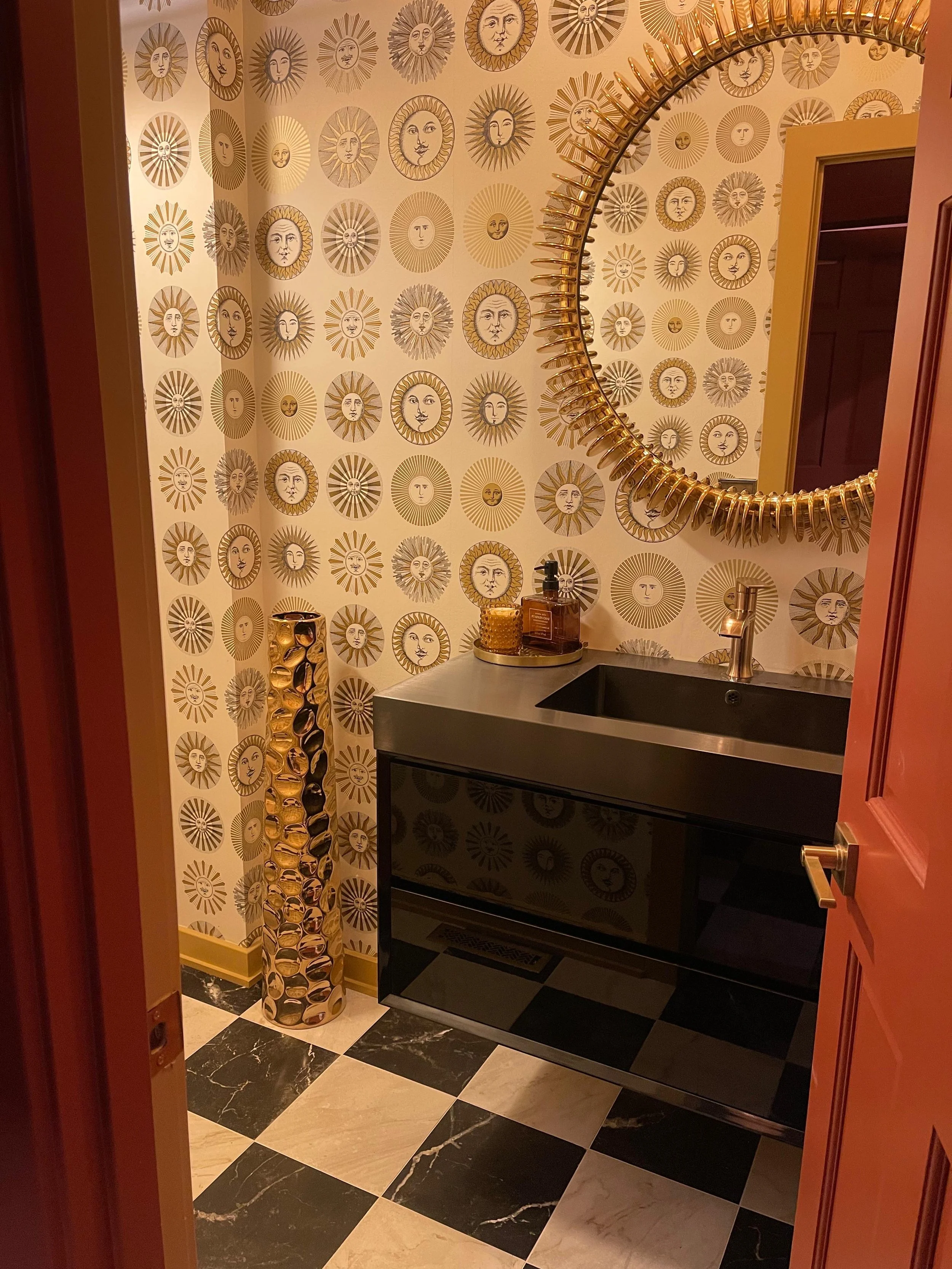 Pink sideboard with gold handles and accents, decorated with bowls, decorative stones, a framed photo, and a vase with cotton branches, against a wall with colorful abstract artwork.