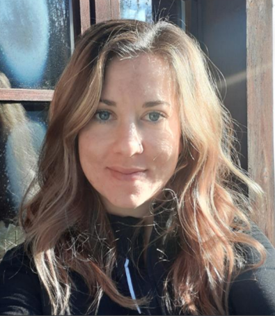 Une femme avec des cheveux longs et ondulés devant une fenêtre en bois, en plein air avec de la lumière naturelle.