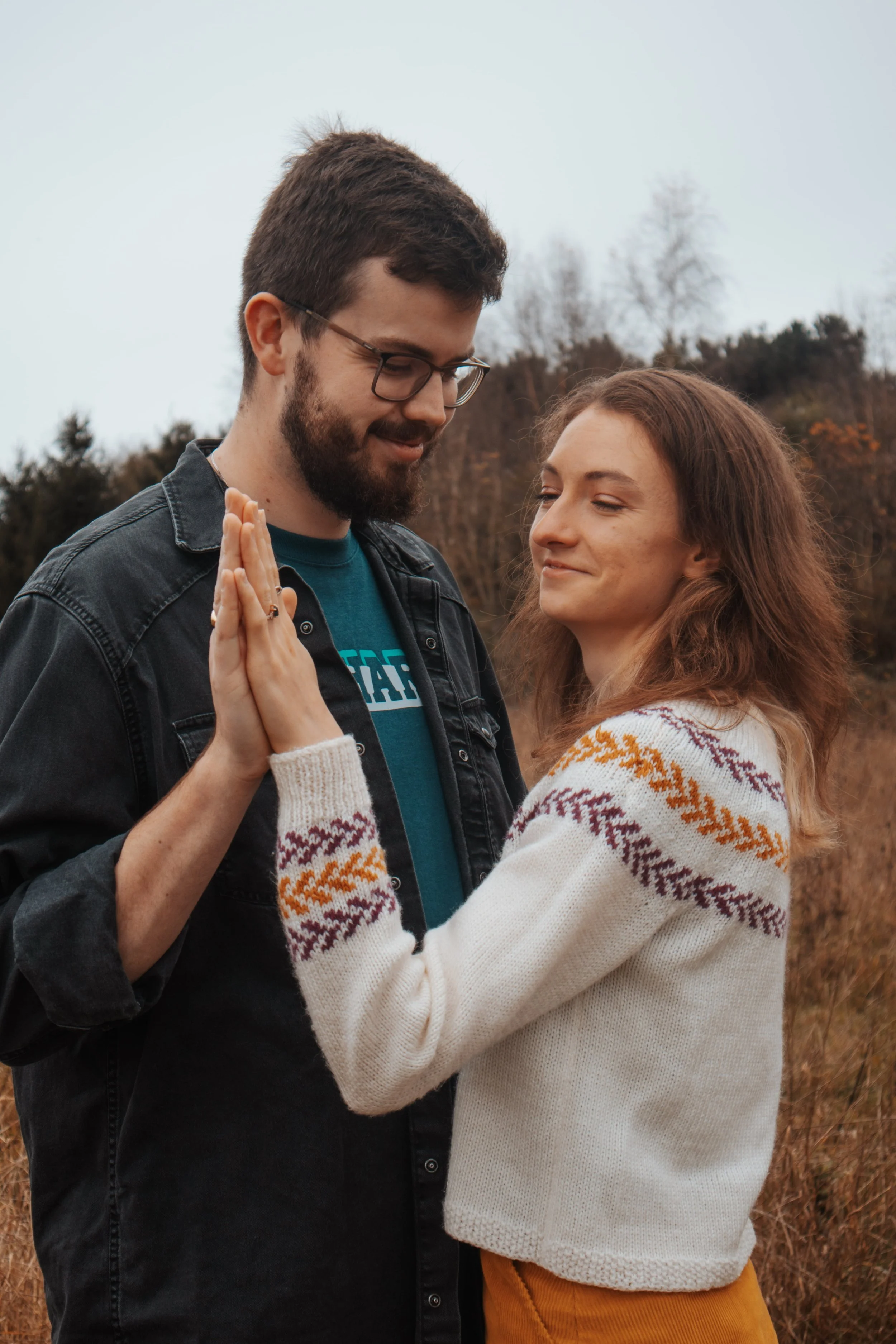A young couple doing a hand heart gesture outdoors on a cloudy day.