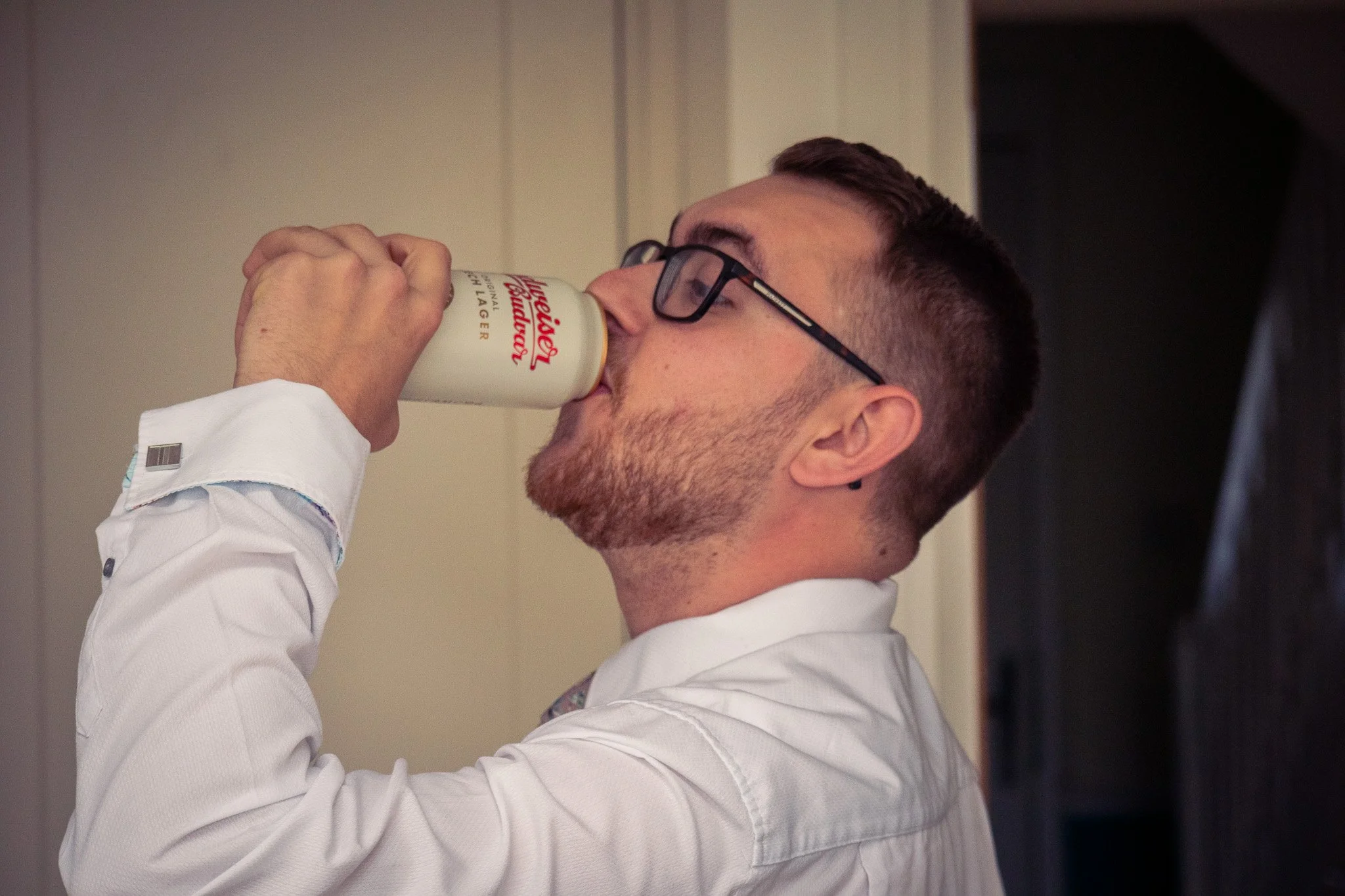A man with glasses and a beard drinking a can of Pabst Blue Ribbon beer.