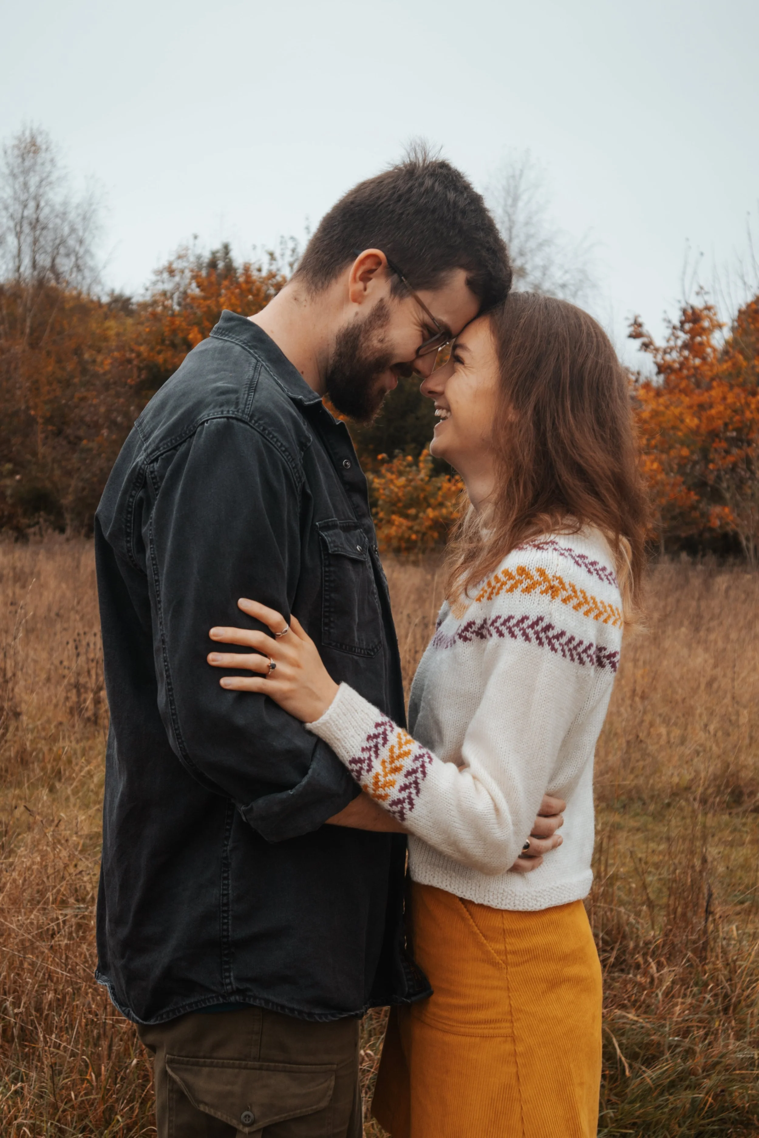 A couple in an autumn field touching foreheads and smiling at each other.