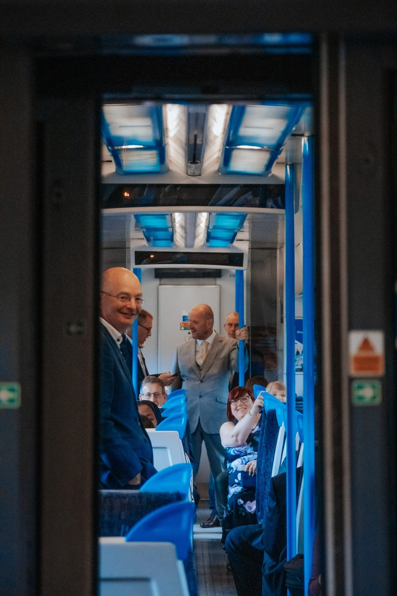 People sitting and standing inside a bus, engaged in conversation, with some smiling and one woman adjusting her purse.