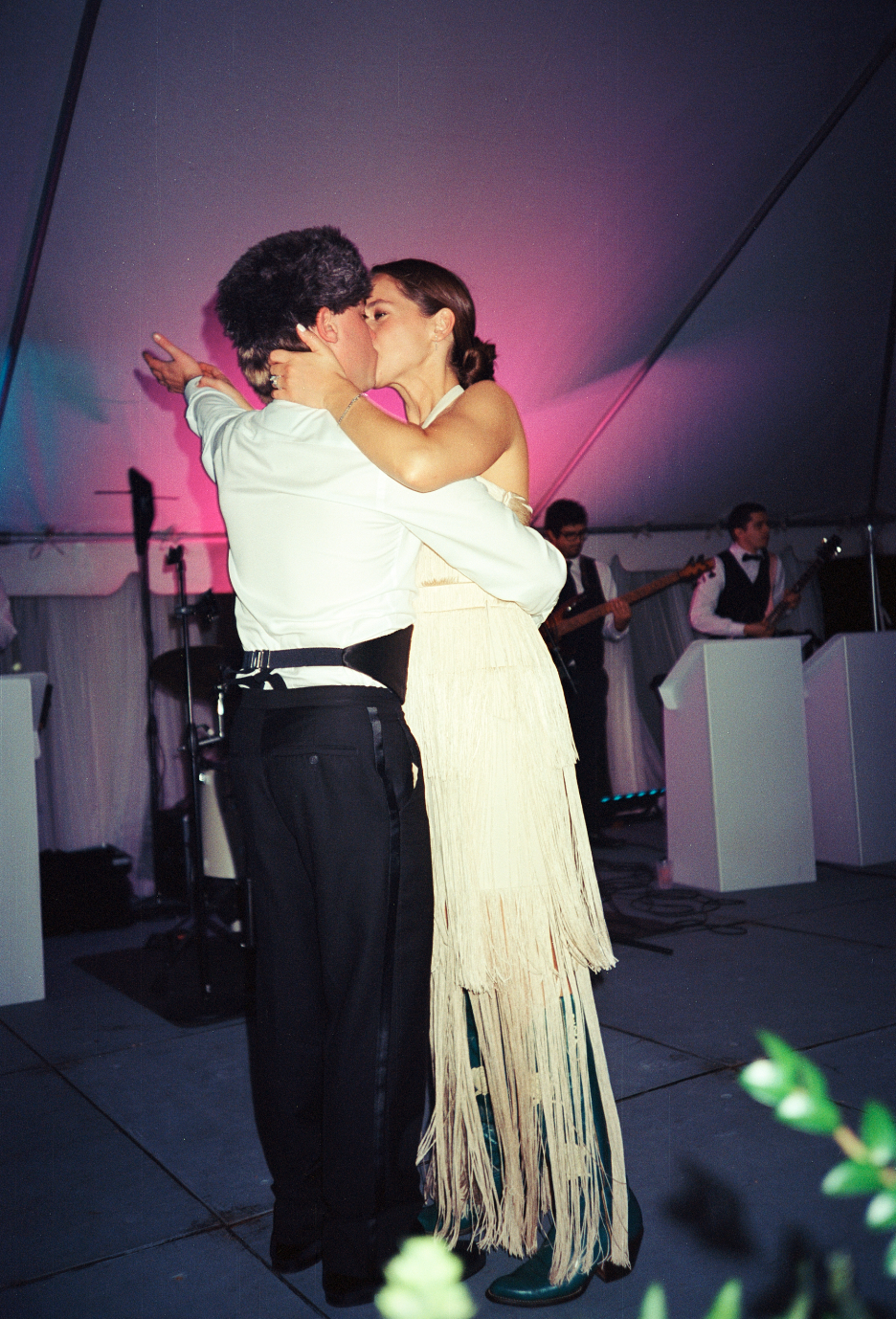 A couple shares a romantic kiss while dancing at a wedding reception with a live band playing in the background.