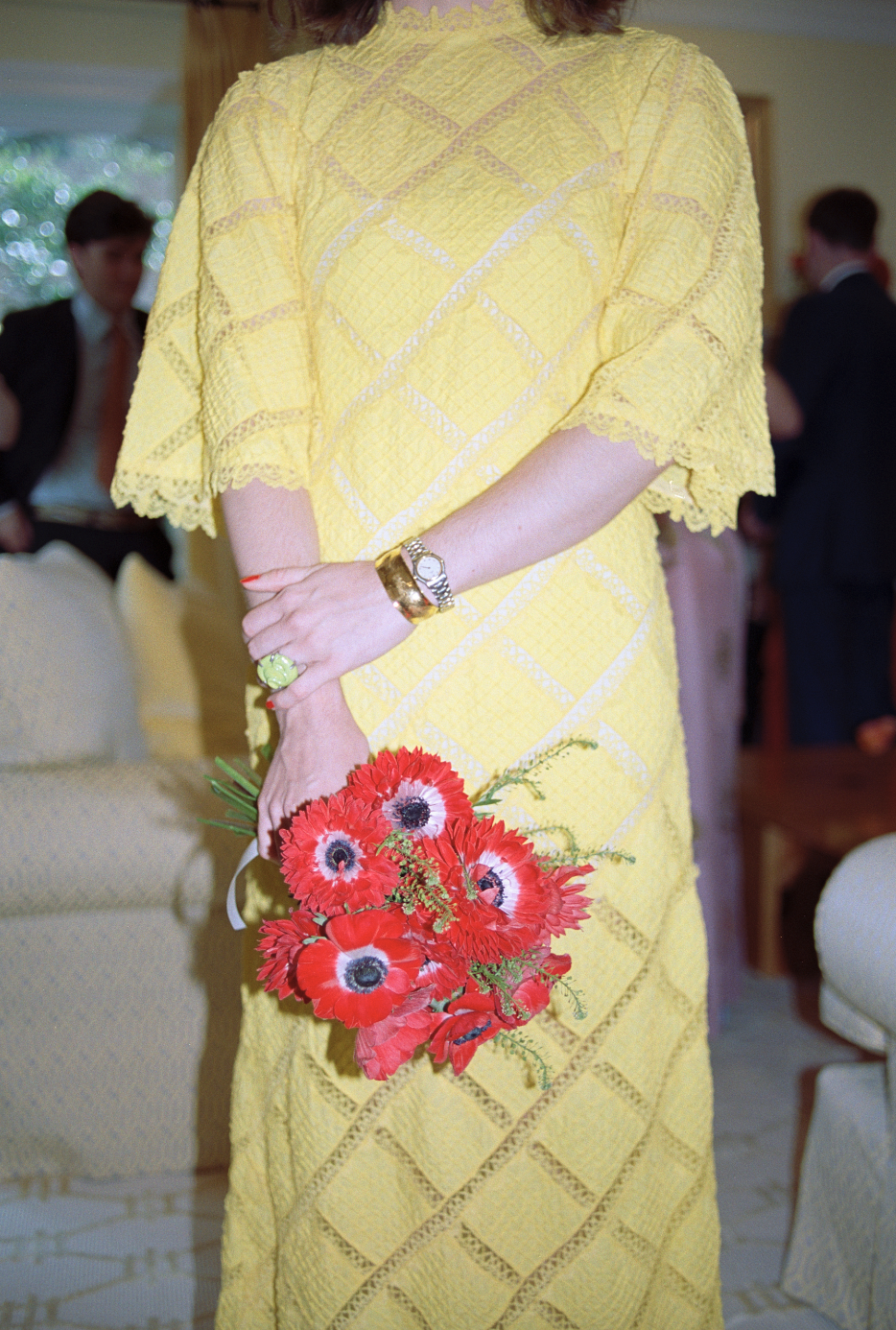 Woman in a yellow dress holding a bouquet of red flowers at a social gathering.